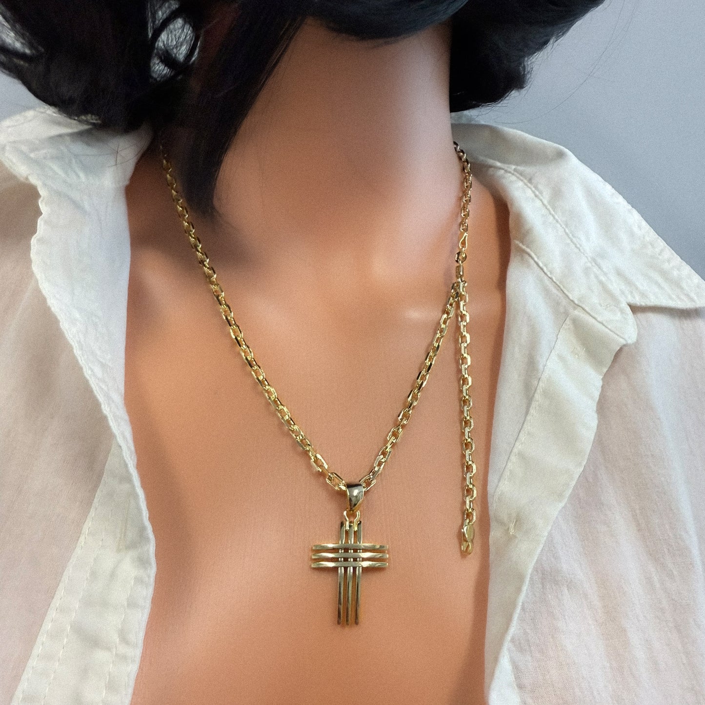 Close-up of a mannequin wearing an 18k gold filled unisex necklace featuring a bold, layered cross pendant and a thick chain, styled with a white open-collar shirt.