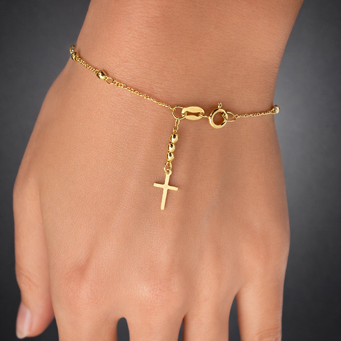 Gold filled cross bracelet on hand, delicate Christian charm bracelet with beaded drop detail, dainty religious jewelry, minimalist gold wrist bracelet studio close up
