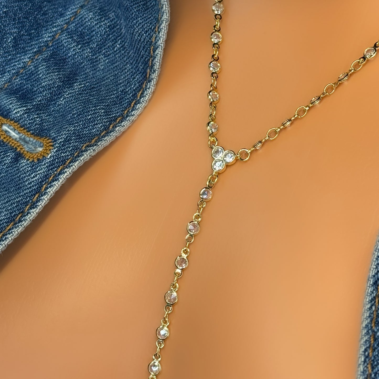 A woman wearing a delicate gold lariat necklace with clear CZ stones under a blue denim jacket, close-up view.