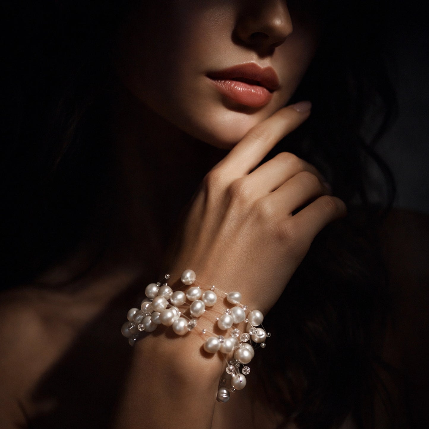 Luxury freshwater pearl cluster bracelet on an elegant female wrist, illuminated by dramatic studio spotlight near the model’s lips and chin. The luminous white pearls and crystal accents glow against smooth skin in a dark, moody background, highlighting the bracelet’s iridescent shine and delicate
