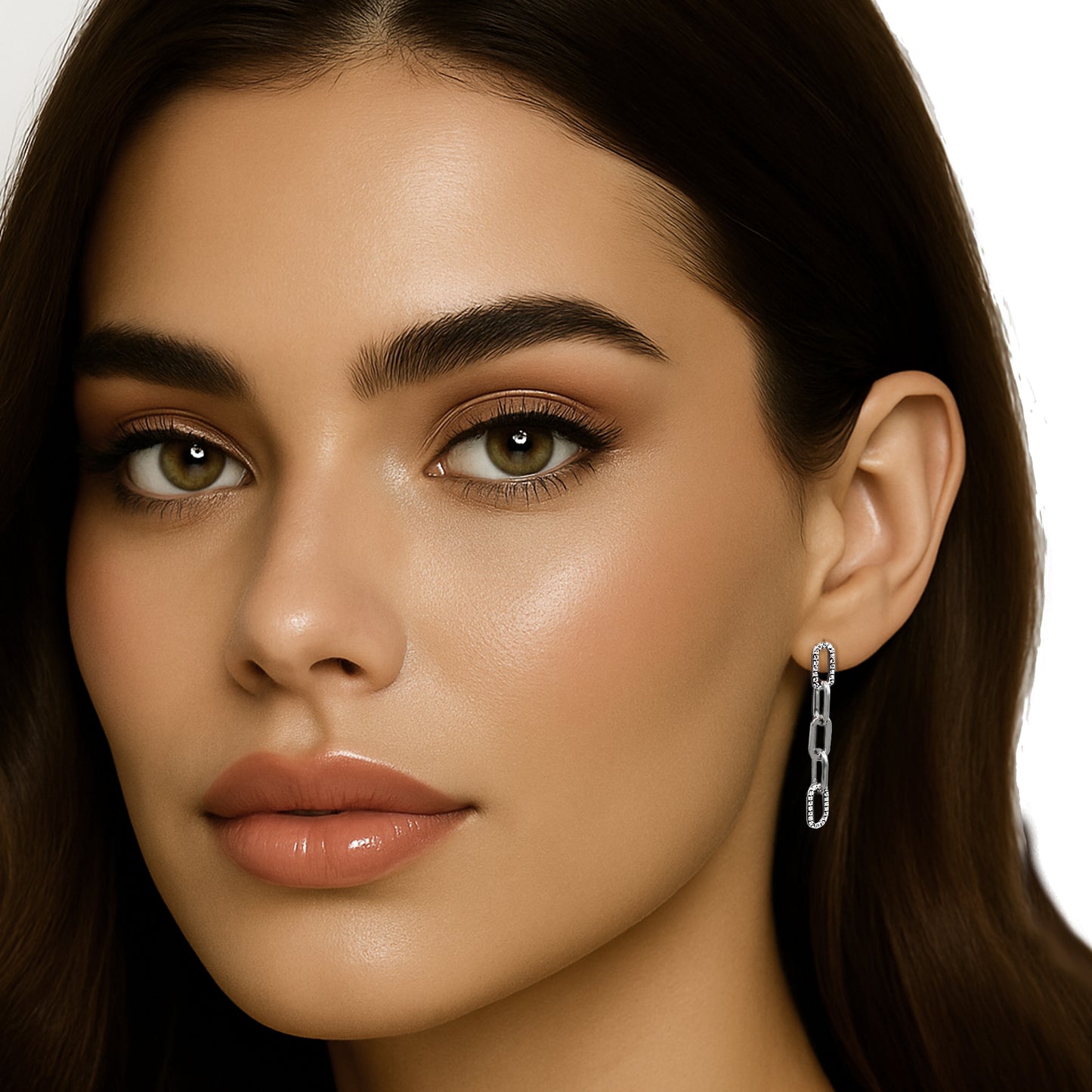 Close-up of a brunette woman wearing long drop earrings featuring cubic zirconia chain links in a vertical design. Her glossy lips and luminous makeup complement the clean white background and centered ear view.