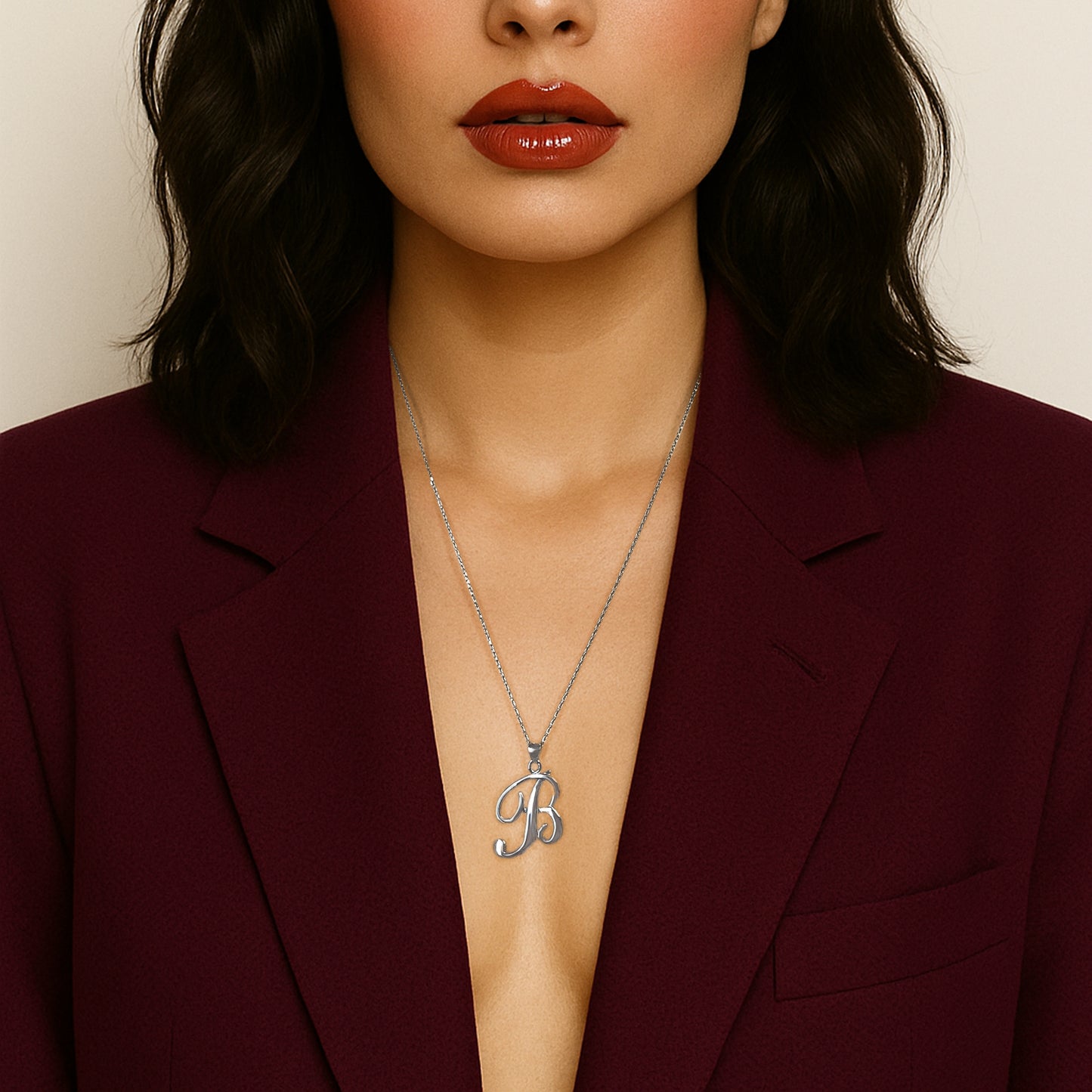 Elegant woman in a deep burgundy blazer with glossy red lips, wearing a delicate yet bold sterling silver large initial pendant necklace with a rhodium finish, creating a modern and sophisticated statement look.