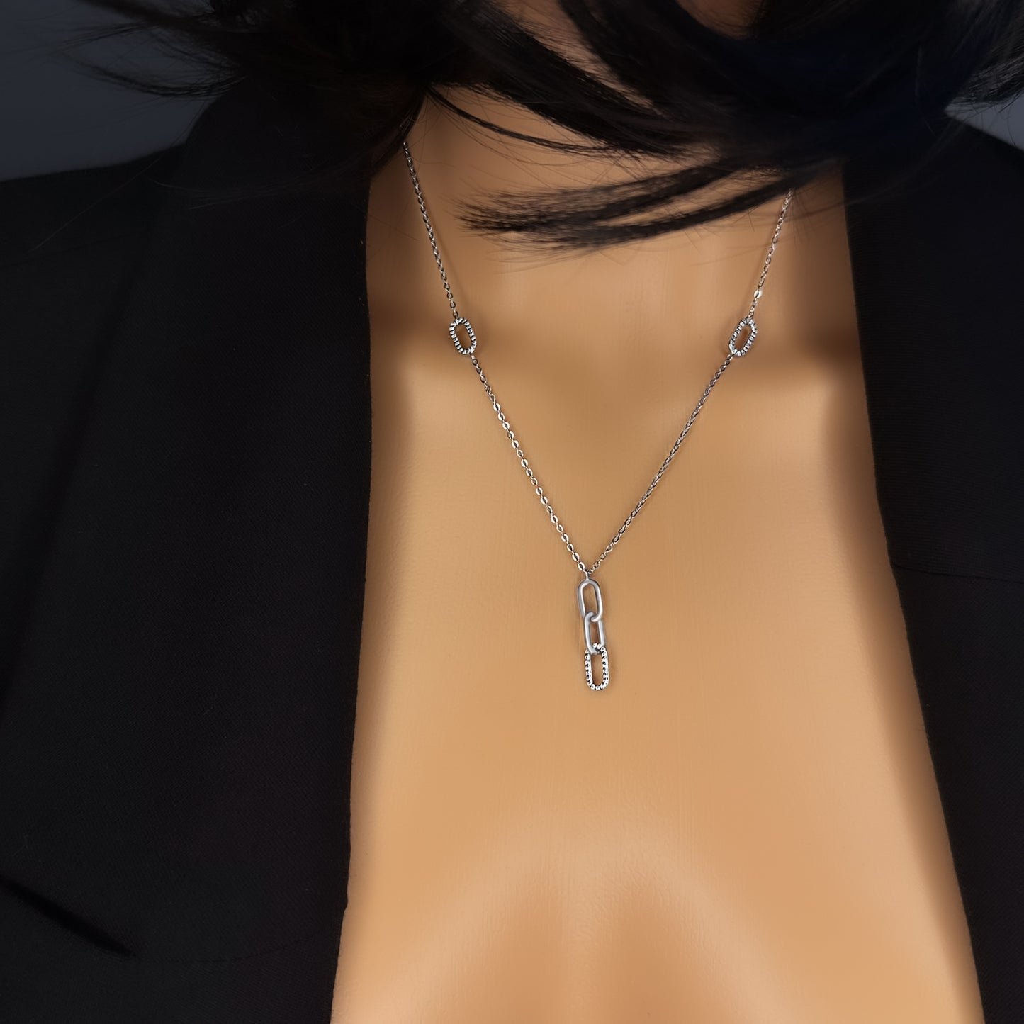 Close-up of a model wearing a sterling silver chain necklace with interlocking paperclip-style links. The center drop features a mix of polished and cubic zirconia-studded links, creating a modern lariat silhouette. Styled with a black blazer and tousled hair.