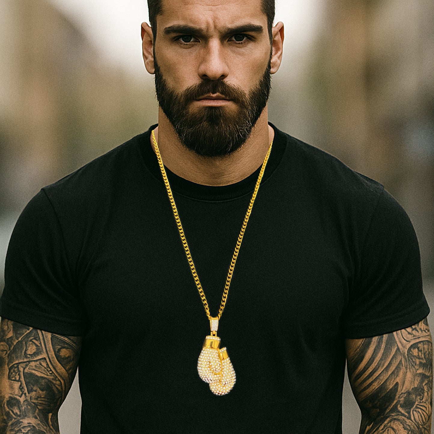 Fit man in black t-shirt showcasing iced out gold boxing glove necklace on thick curb chain, tattooed arms visible