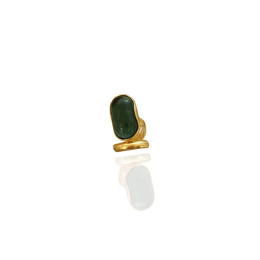 Studio shot of a large gold cocktail ring with a polished deep green gemstone, placed against a white background with a soft reflection underneath.