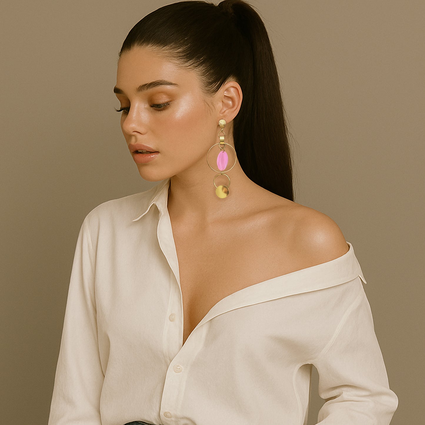Fashionable woman in an off-shoulder white blouse wearing bold mismatched gold hoop earrings with large pink and gold disc accents, styled with a sleek ponytail.