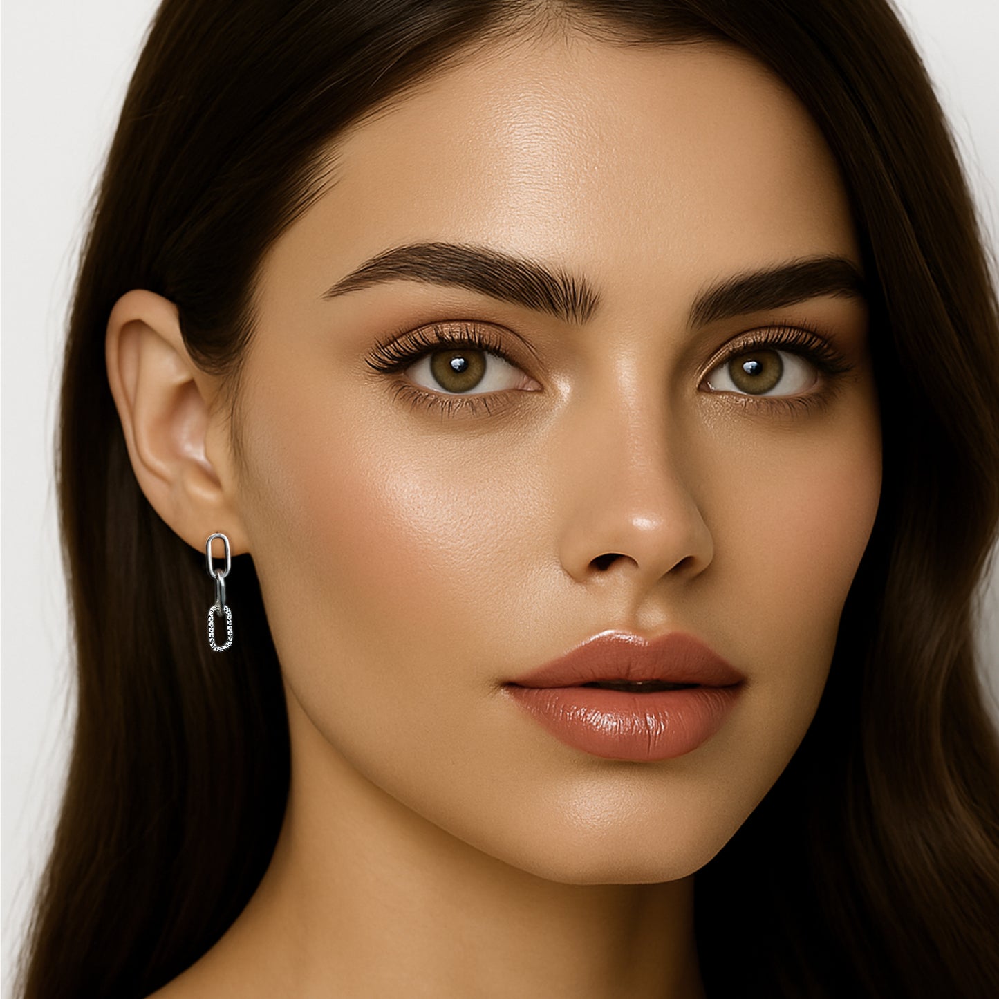 Close-up of a brunette model with minimal makeup wearing mismatched drop earrings in sterling silver with CZ accents. One ear shows a bold chain link drop; the other displays a smaller link design, all set against a white backdrop.