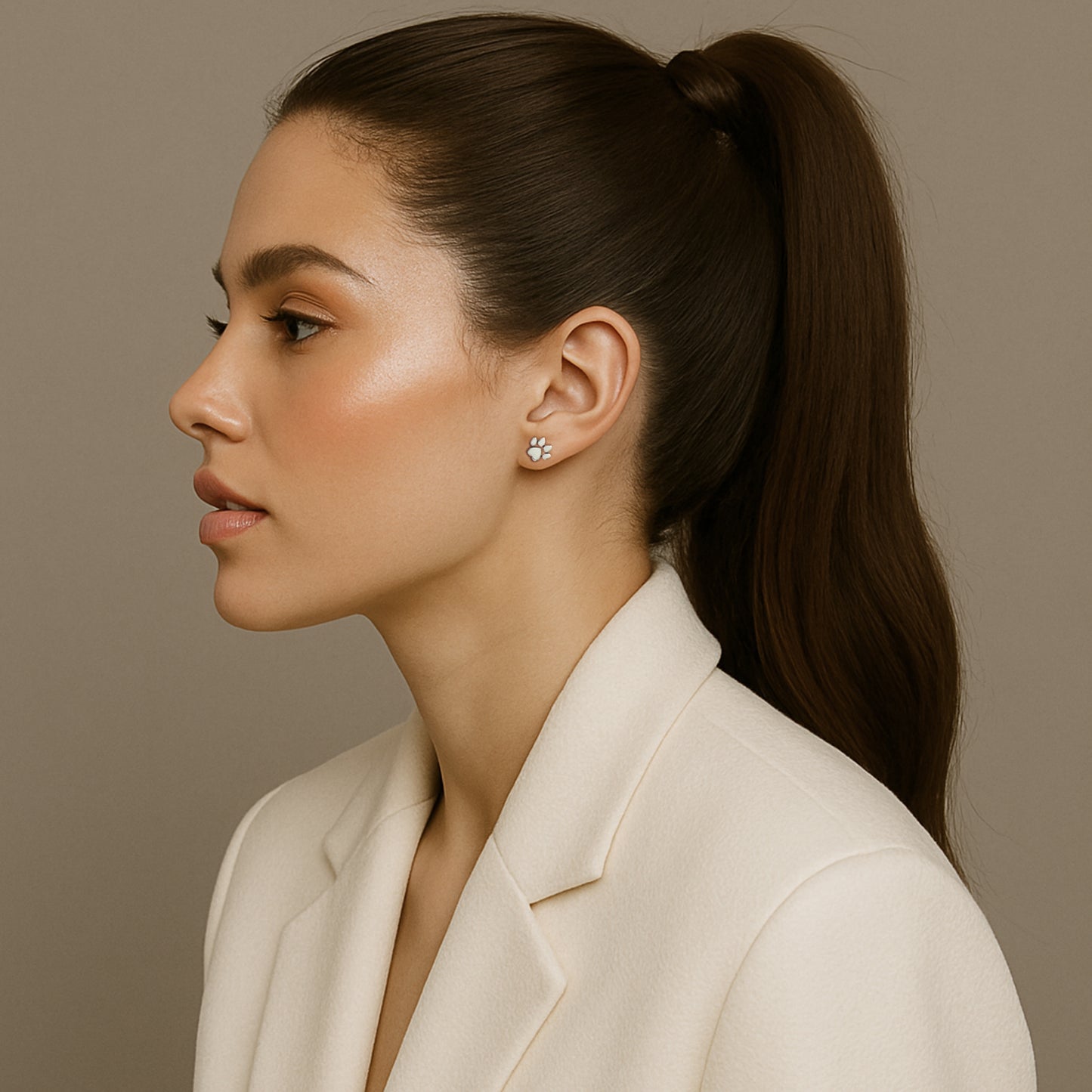 Elegant woman in a cream blazer wearing sterling silver paw print stud earrings, shown in profile with sleek ponytail and soft glam makeup.