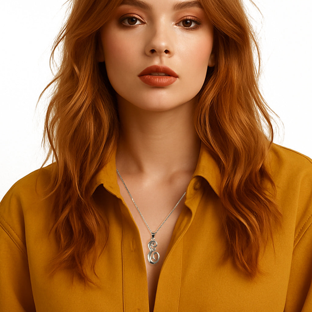 Stylish red-haired woman in a mustard button-down shirt wearing a bold sterling silver initial pendant necklace with intertwined modern letter shapes, creating a statement yet elegant look.