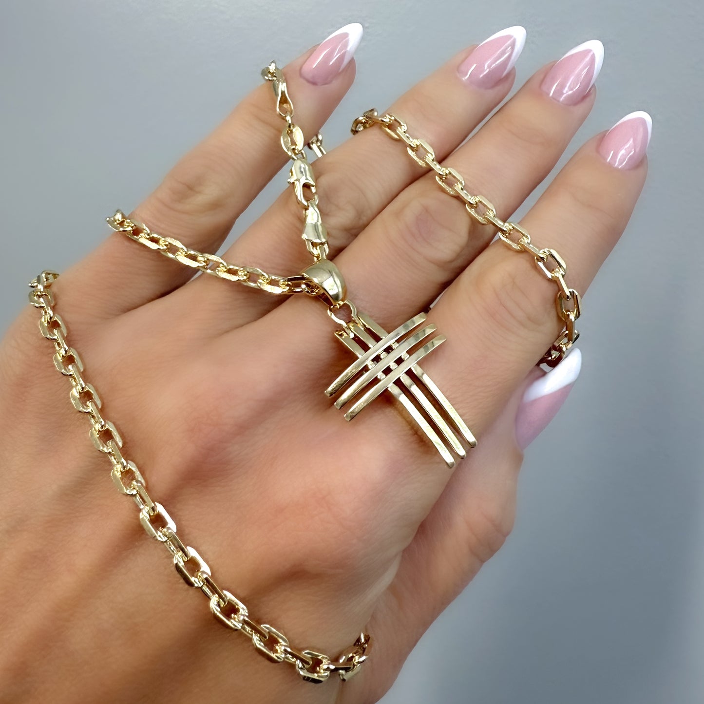 Hand holding a bold gold chain necklace with a modern, layered bar cross pendant, displayed against a neutral background.