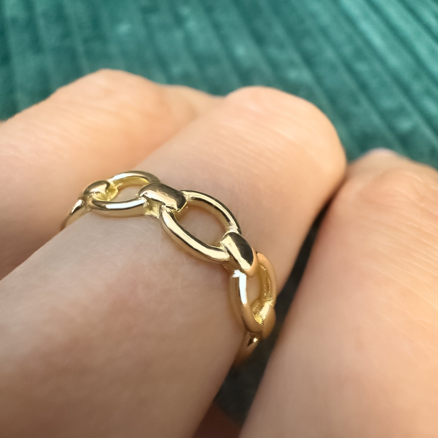 Side view of a gold link ring on finger, capturing light and detail of each rounded link in a soft natural light.