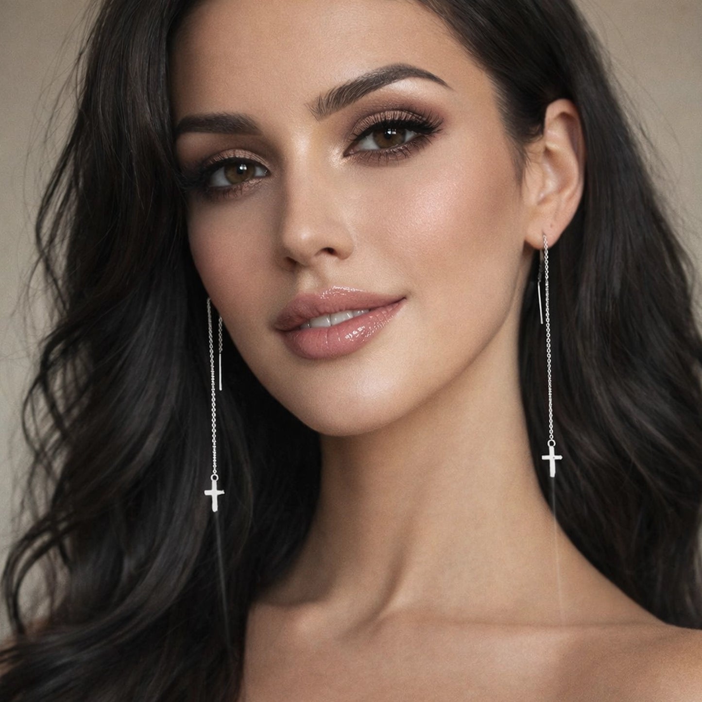 Elegant studio portrait of a beautiful woman wearing long silver pull-through threader earrings with delicate chain drops and small cross charms, shown from the shoulders up against a soft neutral background, highlighting the earrings’ length, shine, and minimalist religious design.