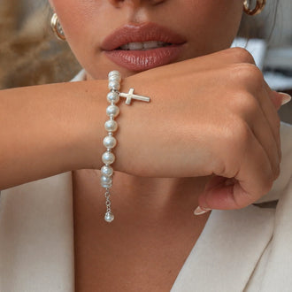 Elegant pearl bracelet with silver cross charm on model wrist, dainty religious jewelry for everyday wear and meaningful gifting