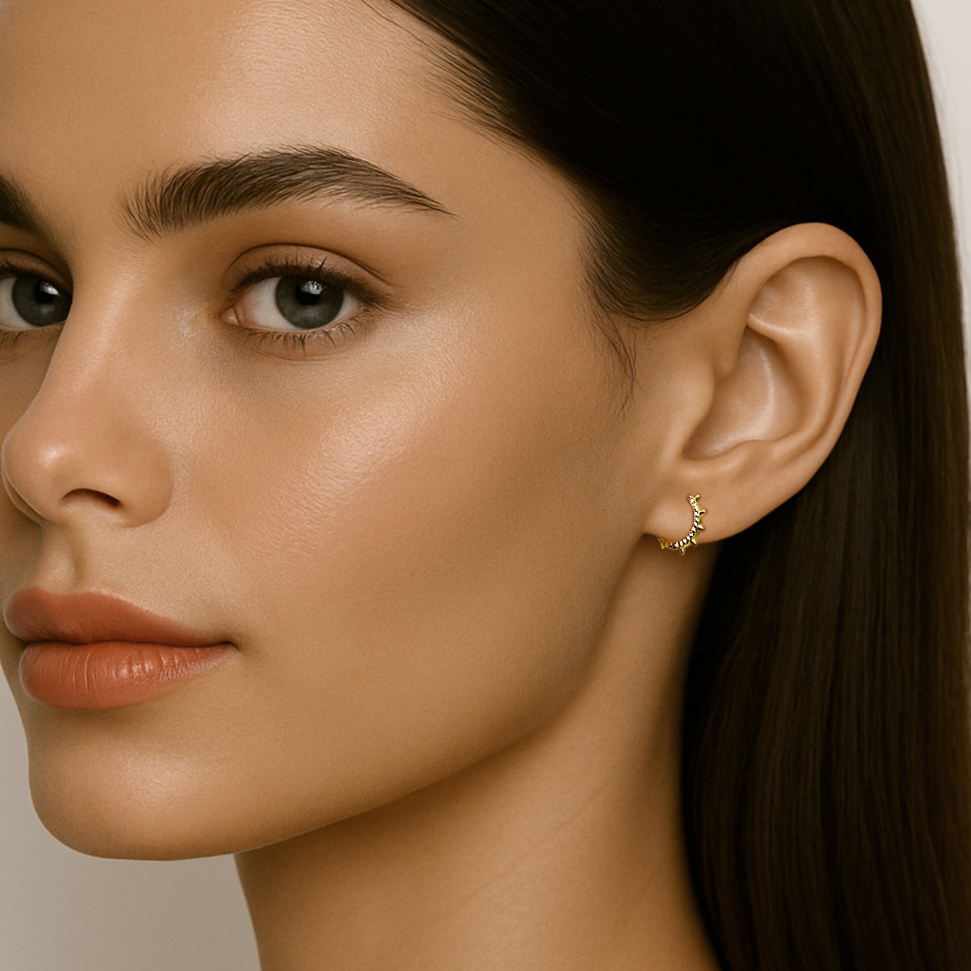 Close-up of a woman wearing a small 18k gold filled spike hoop earring with cubic zirconia detail on her earlobe; the earring forms a delicate circle with mini spikes and subtle sparkle.