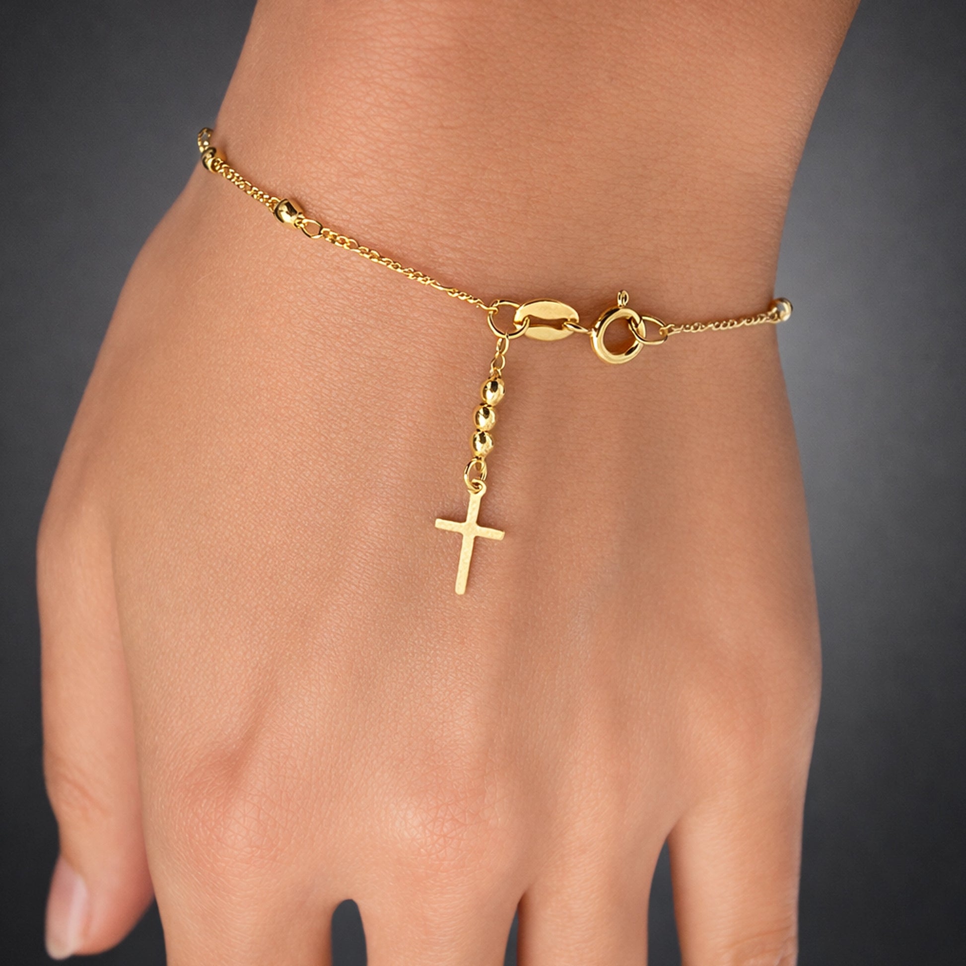 Gold filled cross bracelet on hand, delicate Christian charm bracelet with beaded drop detail, dainty religious jewelry, minimalist gold wrist bracelet studio close up
