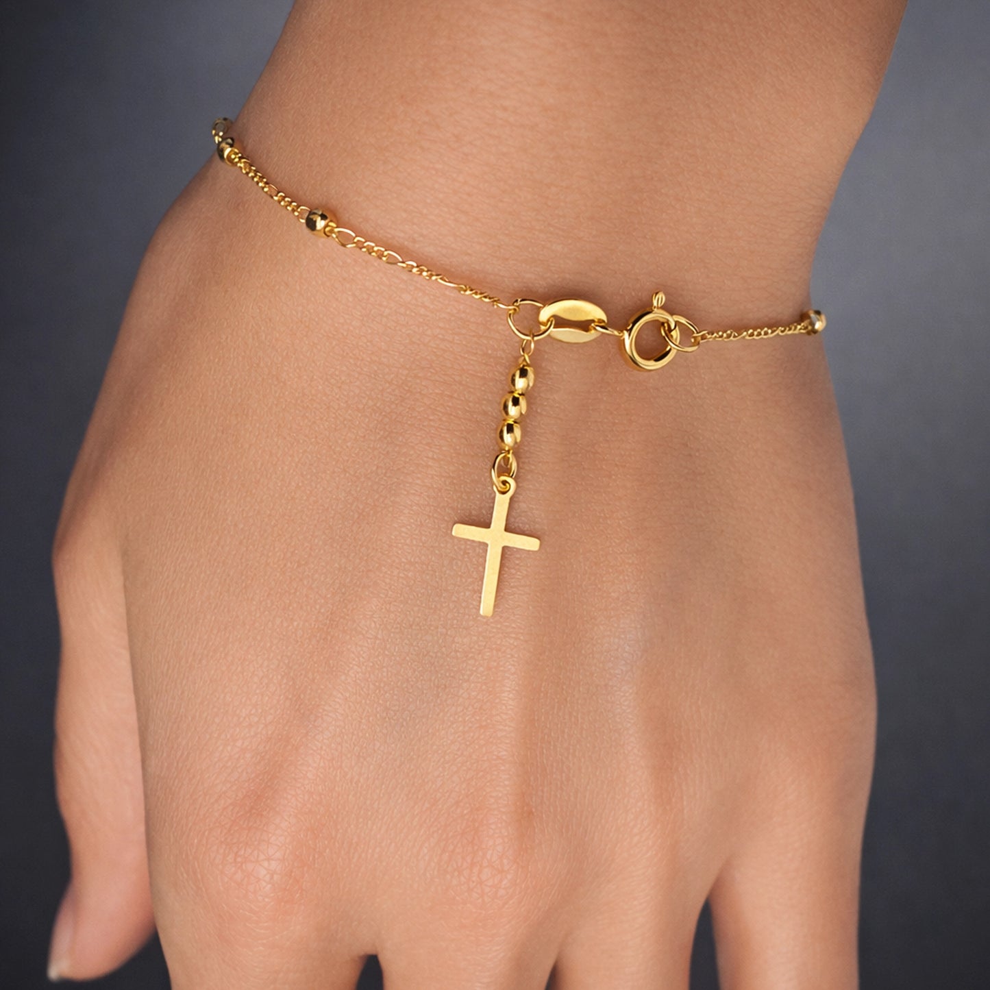 Gold cross bracelet on hand, delicate 18K gold filled chain bracelet with small beads and cross charm, minimalist Christian jewelry, dainty everyday faith bracelet, studio close-up on smooth skin.