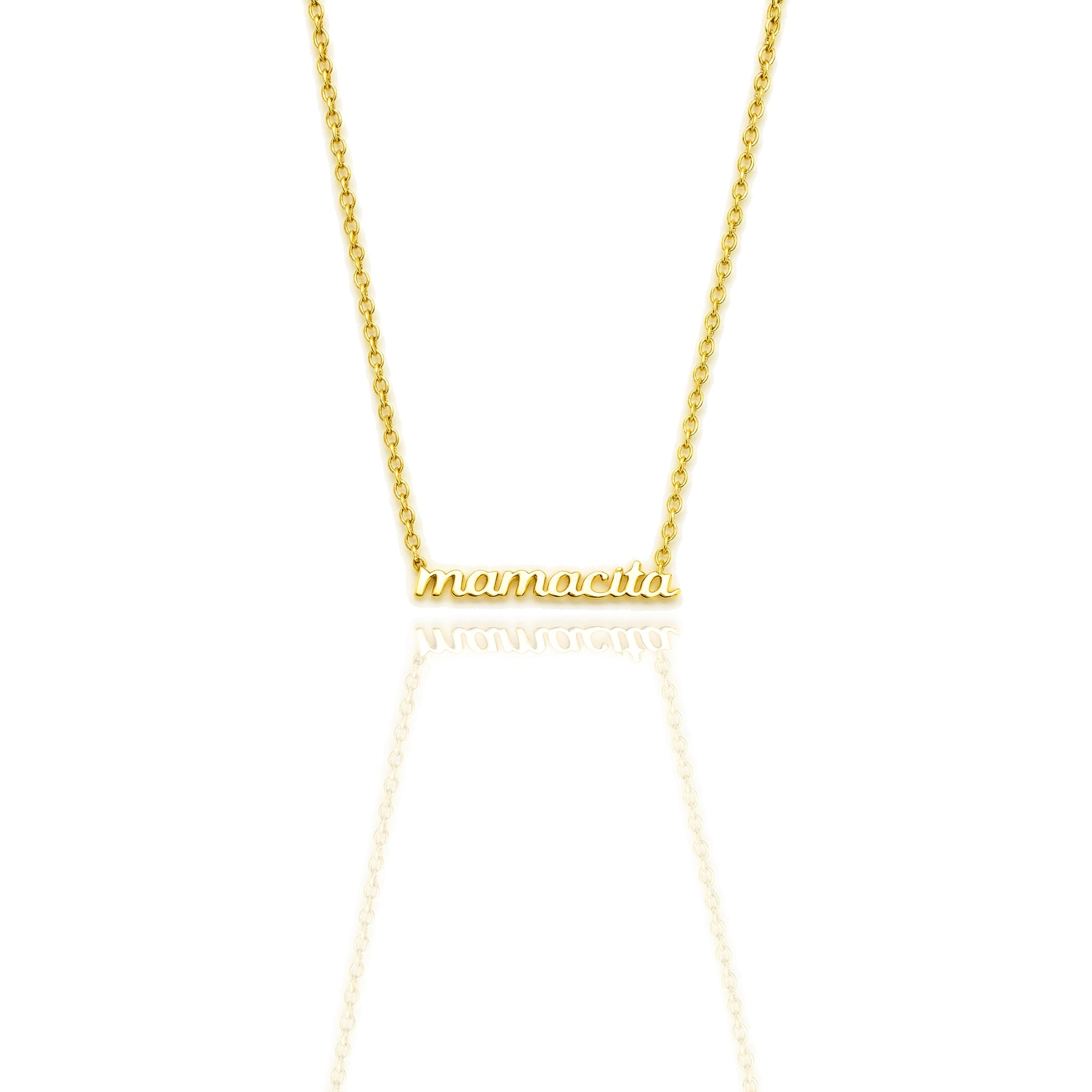 Close-up of an 18K gold filled necklace with “mamacita” in polished script font on a dainty cable chain, shown on a white reflective background.