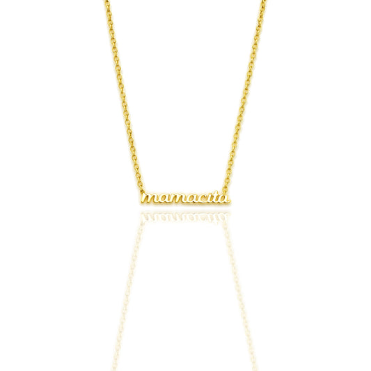 Close-up of an 18K gold filled necklace with “mamacita” in polished script font on a dainty cable chain, shown on a white reflective background.