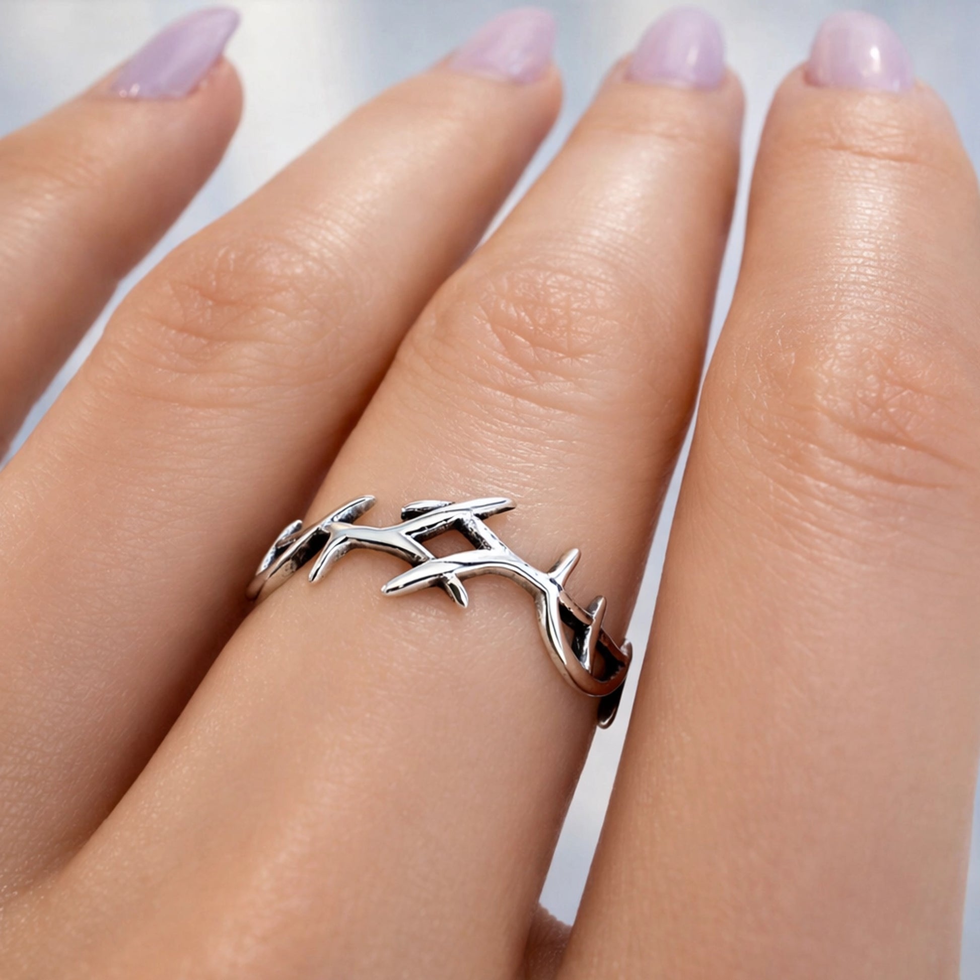 Sterling silver crown of thorns ring worn on a hand with soft lilac manicure, showcasing a delicate Christian band with thorny vine design symbolizing Jesus' sacrifice.