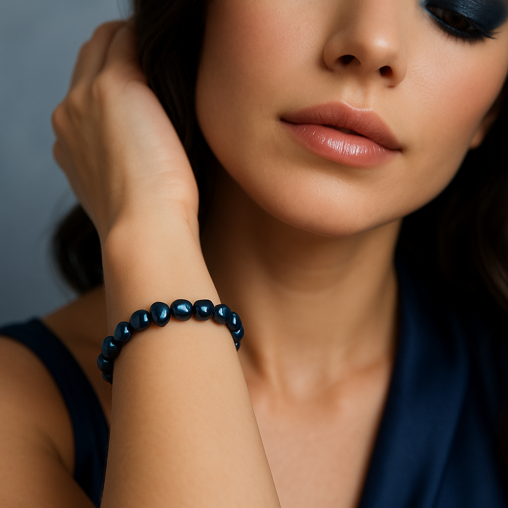 Close-up of a model’s wrist wearing an elastic dark-blue baroque freshwater pearl bracelet - small irregular vertical-oval/flat pearls with iridescent navy sheen - centered; smoky-eye makeup softly blurred.