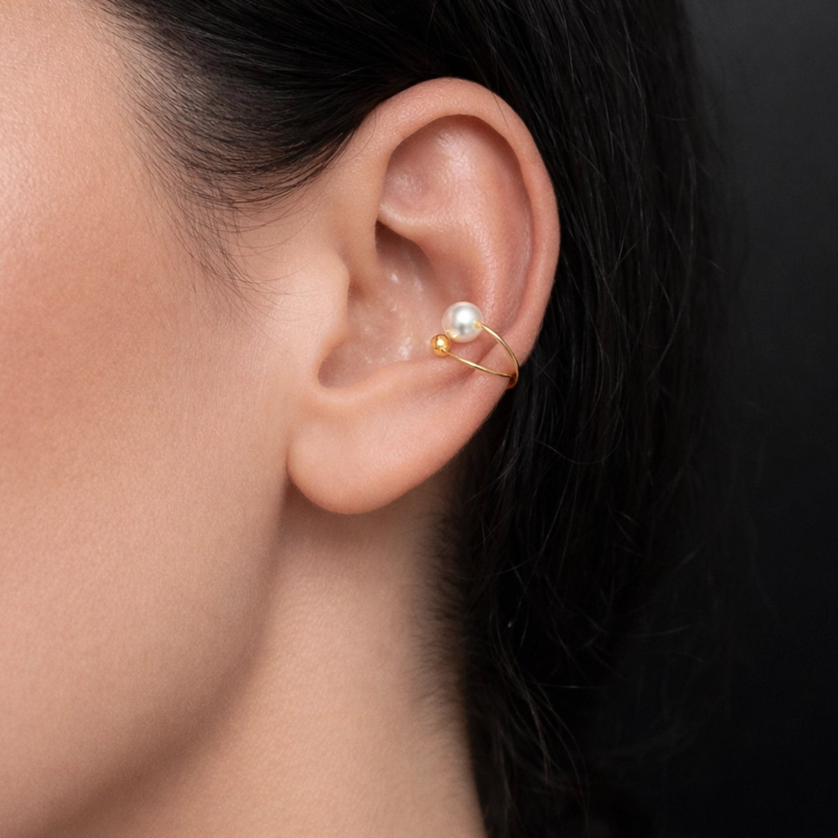Gold pearl ear cuff earring with a delicate gold bead and white pearl accent, worn on the upper ear in a close-up studio photo. This minimalist gold ear cuff with pearl creates an elegant, modern look without a piercing, perfect for dainty everyday jewelry and layered ear styling.