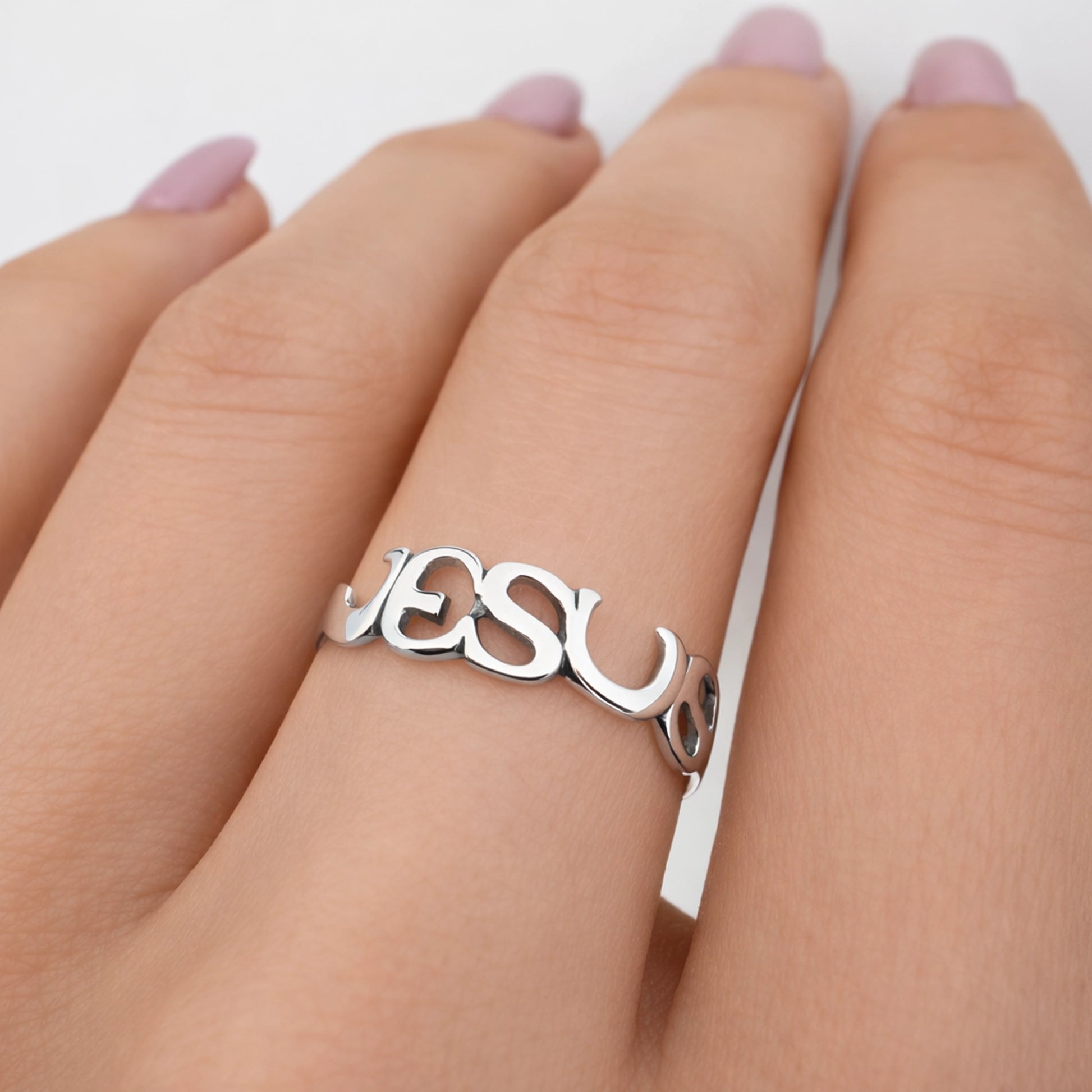 Polished sterling silver JESUS script ring on a woman’s finger, close-up view showing smooth connected lettering, mirror-like shine, natural skin tones, and a clean studio white background.