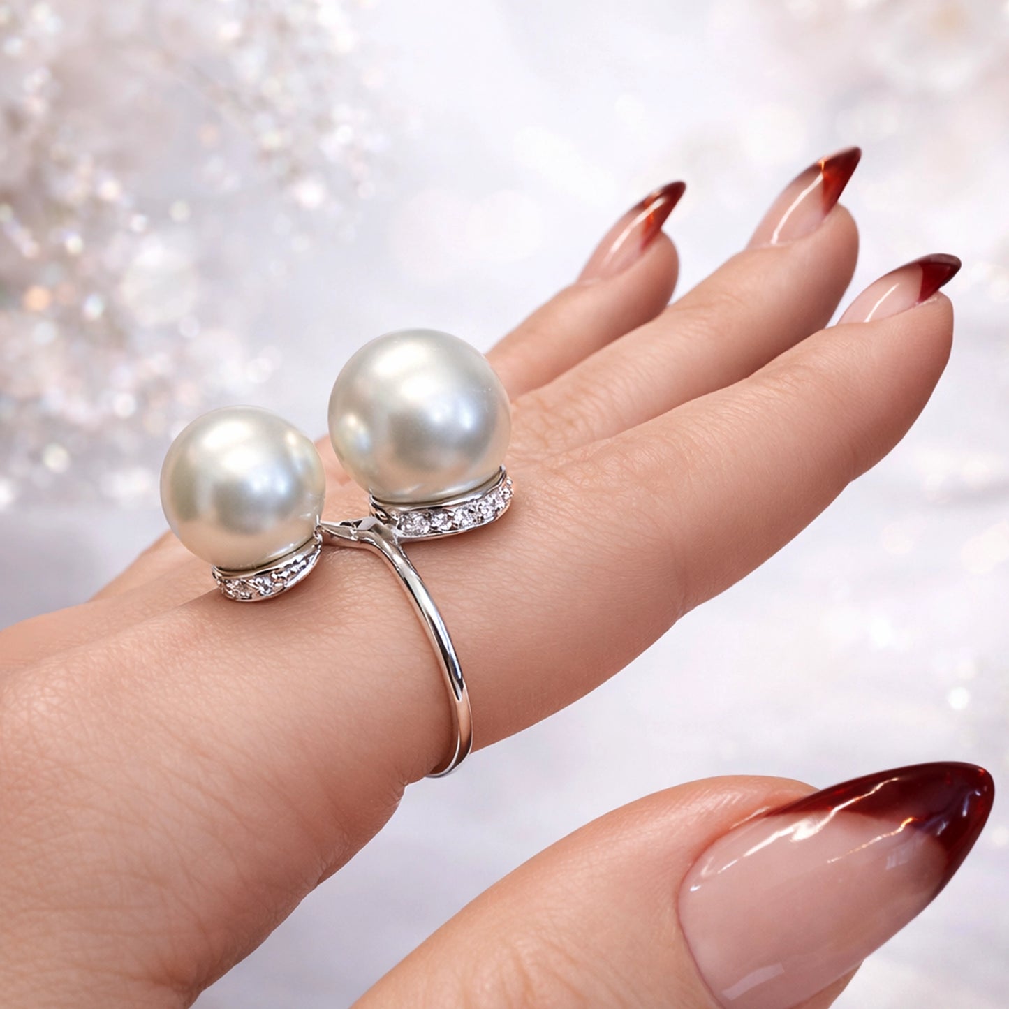 Open adjustable pearl ring on hand, featuring two pearls of different sizes with sparkling pavé stones, polished silver band, elegant manicure, soft professional studio background, luxury jewelry close-up.