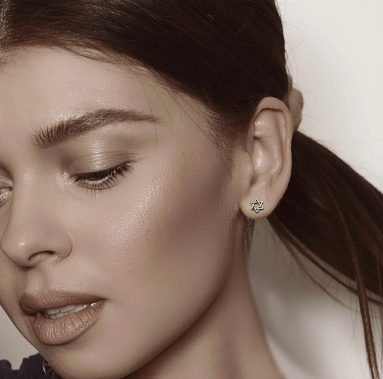 Close-up of a woman wearing a small stud earring with a star of David design.