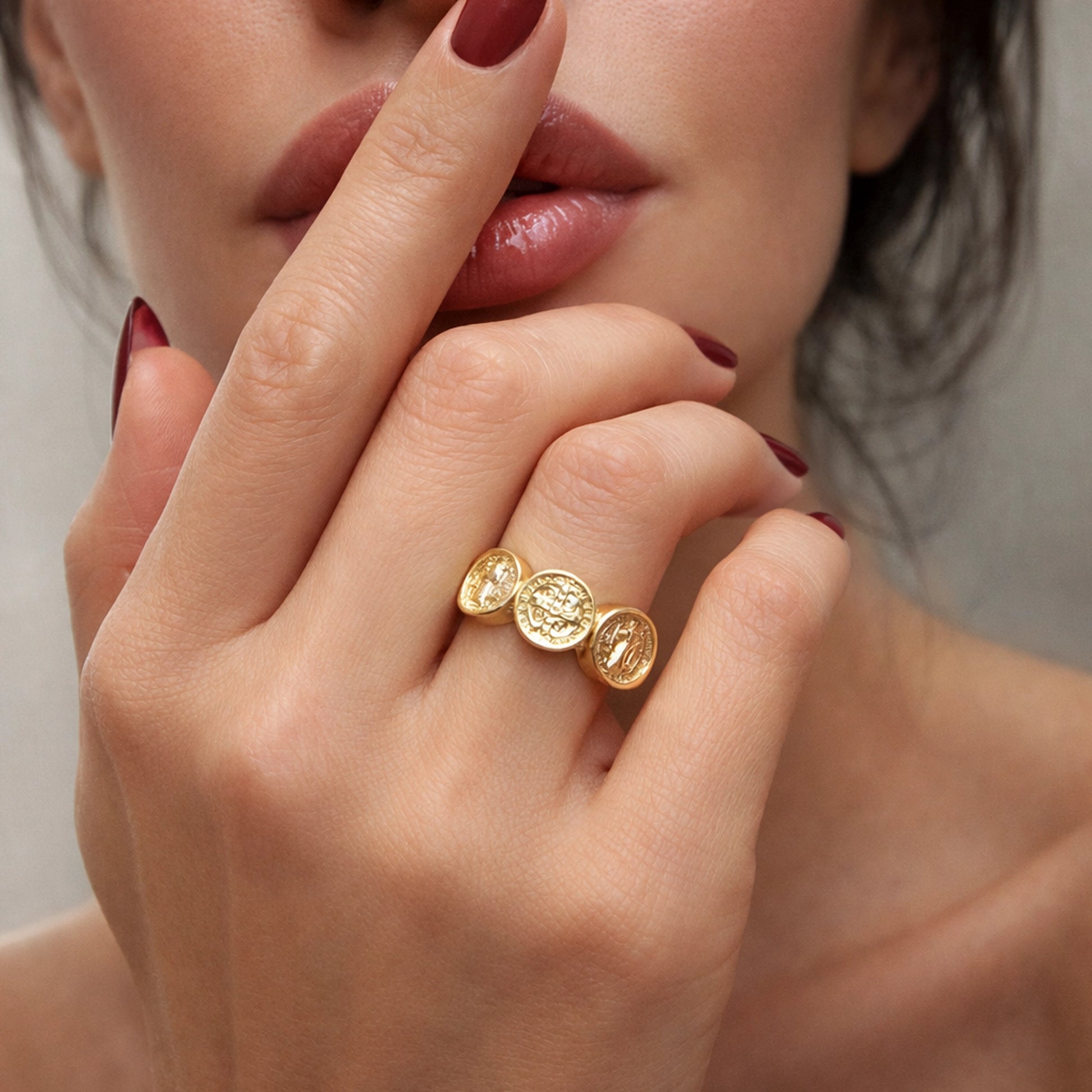 Gold coin ring on woman’s hand, close-up lifestyle photo with soft natural skin tones, glossy lips, elegant manicure, and minimalist studio background, luxury jewelry styling, square image.