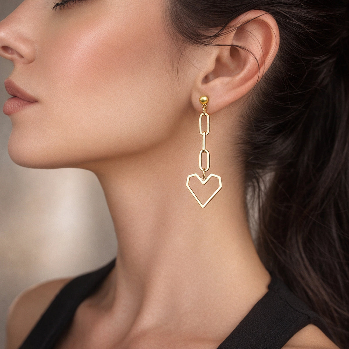 Asymmetrical heart chain earrings worn on ear, gold drop earring with chain link and open heart charm, trendy mismatched earrings close-up on model
