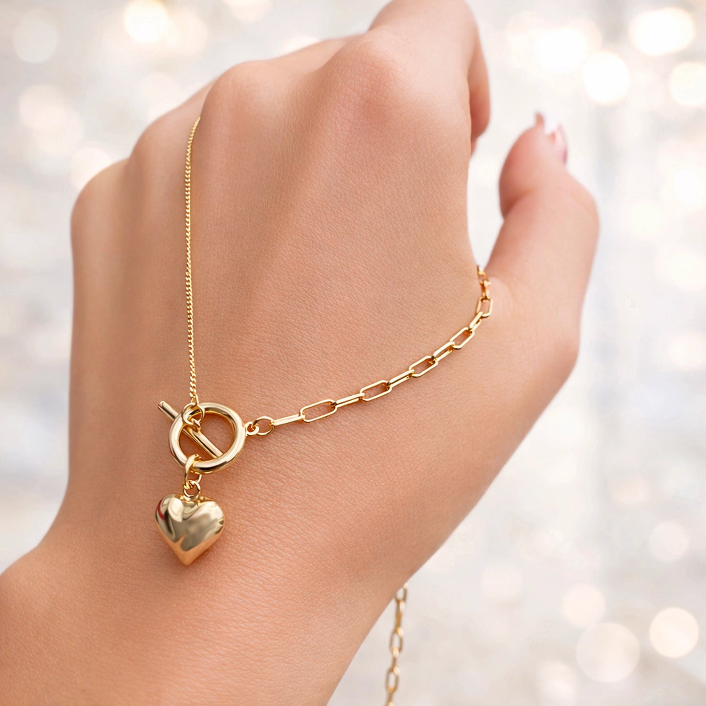 Gold necklace with a heart pendant on a hand against a blurred light background