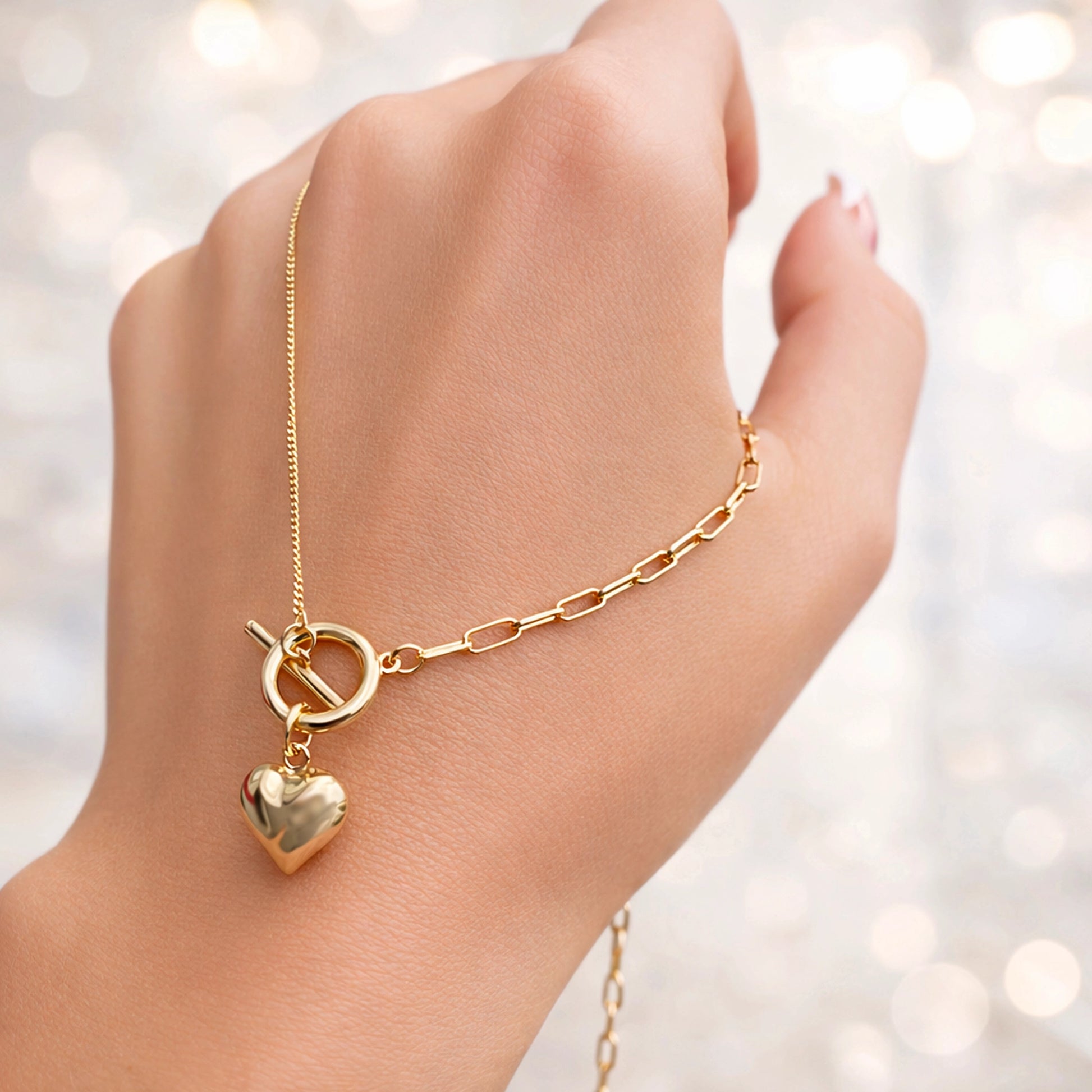 Gold necklace with a heart pendant on a hand against a blurred light background