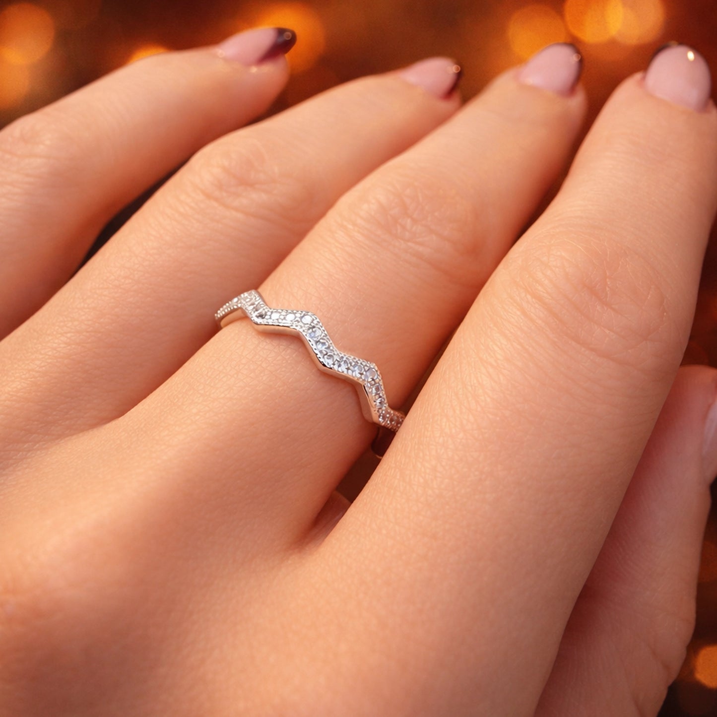 Sterling silver chevron zigzag ring with sparkling cubic zirconia stones on a woman’s hand, elegant minimalist stackable wave ring with delicate pavé CZ, modern fine jewelry close-up.