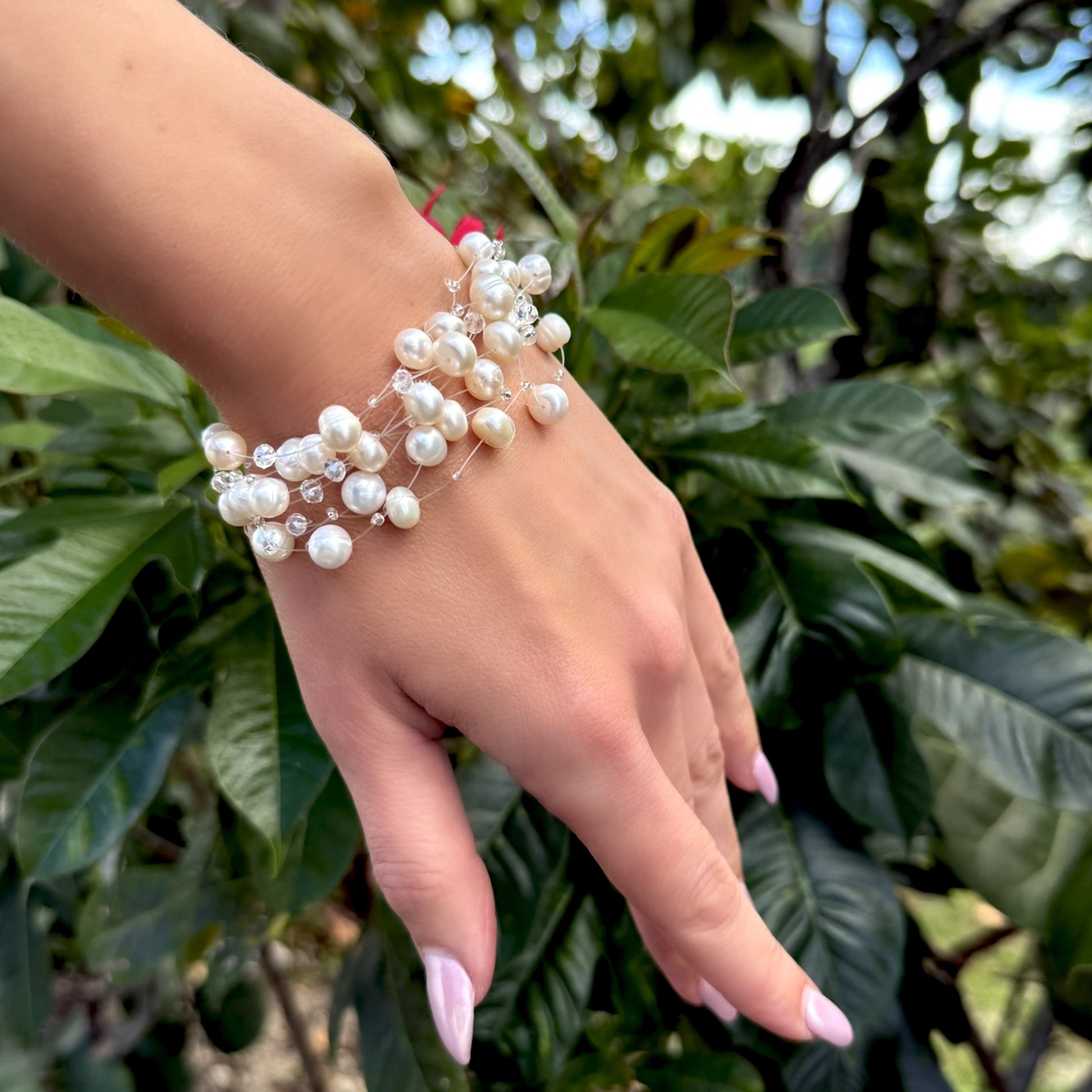Handmade freshwater pearl bracelet with crystals shown from a side angle on an outstretched hand, surrounded by tropical greenery.