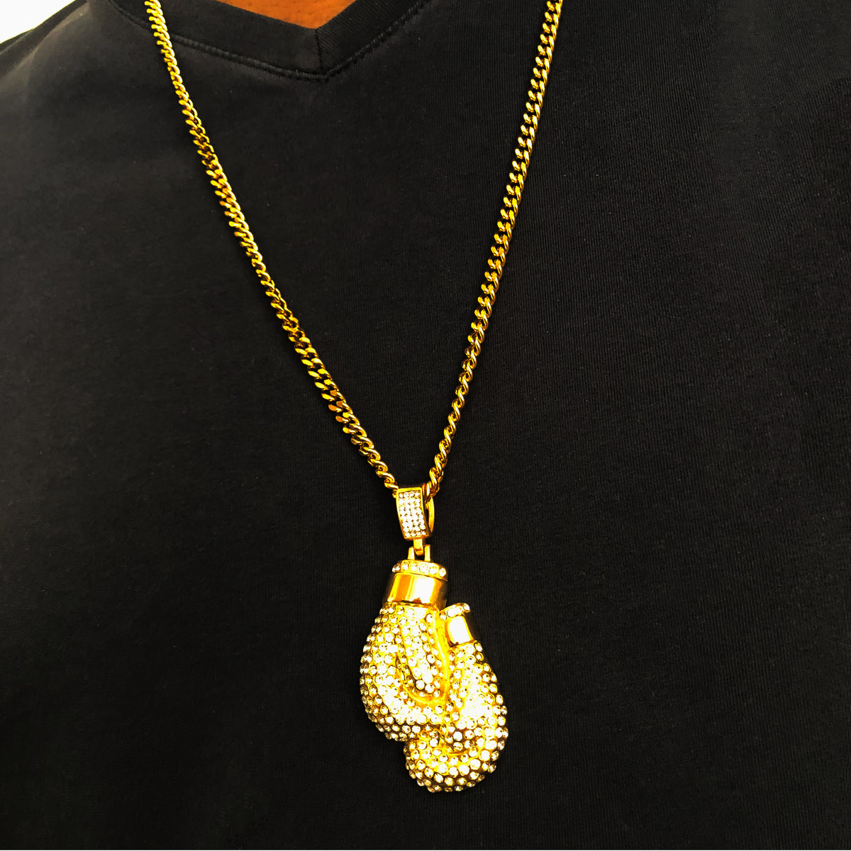 Men’s boxing gloves necklace with gold Cuban chain and crystal detailing, worn over a black V-neck shirt