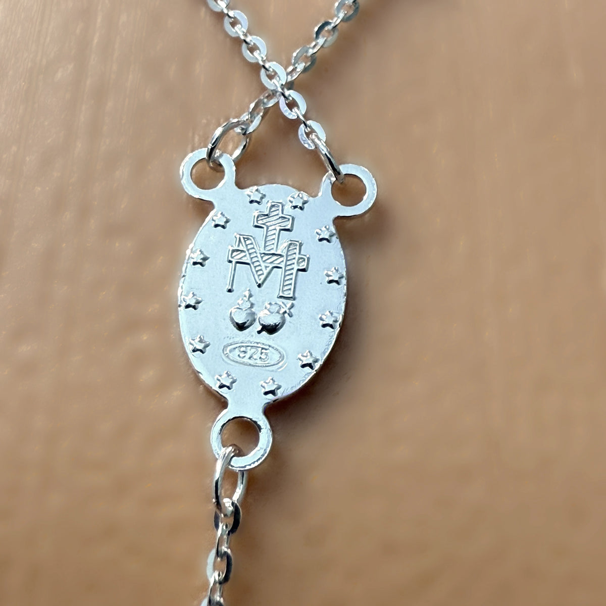 Close-up of the back side of a sterling silver Miraculous Medal showing engraved symbols and 925 stamp on a fine cable chain.