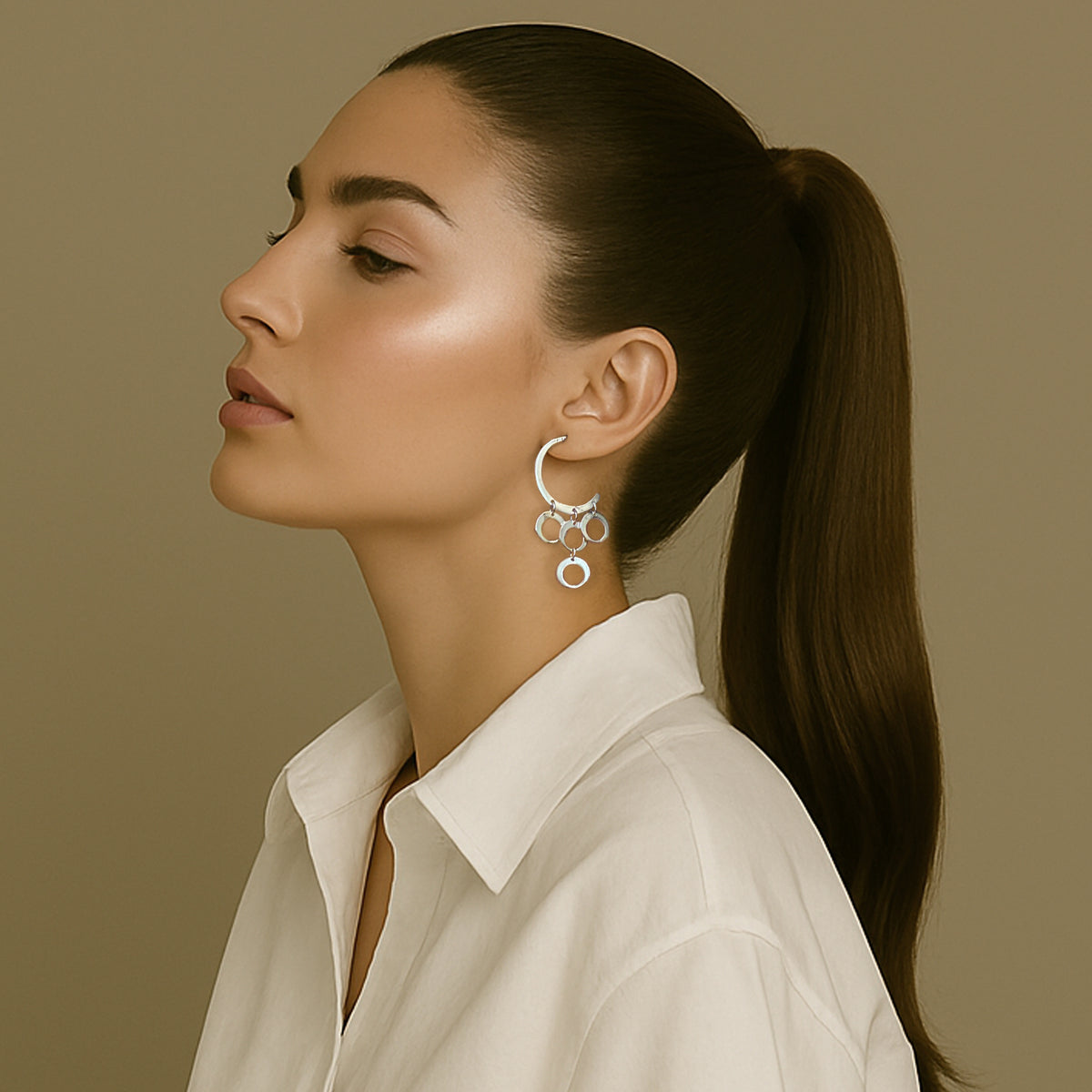 Stylish woman with sleek ponytail wearing a white collared shirt and bold sterling silver chandelier earrings with interlinked hoops in a crescent design.