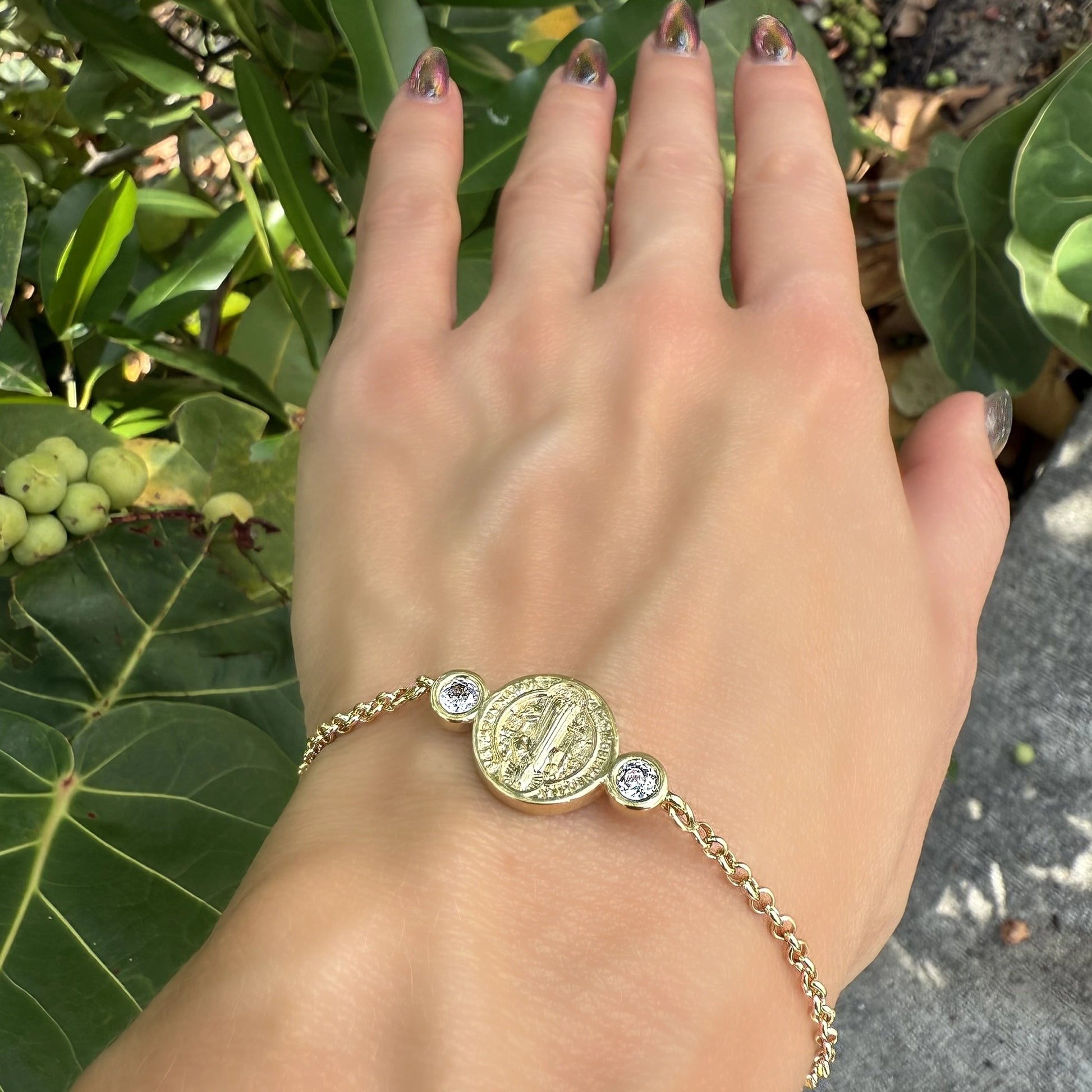 Shimmering Saint Benedict gold medallion bracelet with round CZ accents, photographed under natural sunlight highlighting the chain detail and medallion texture.