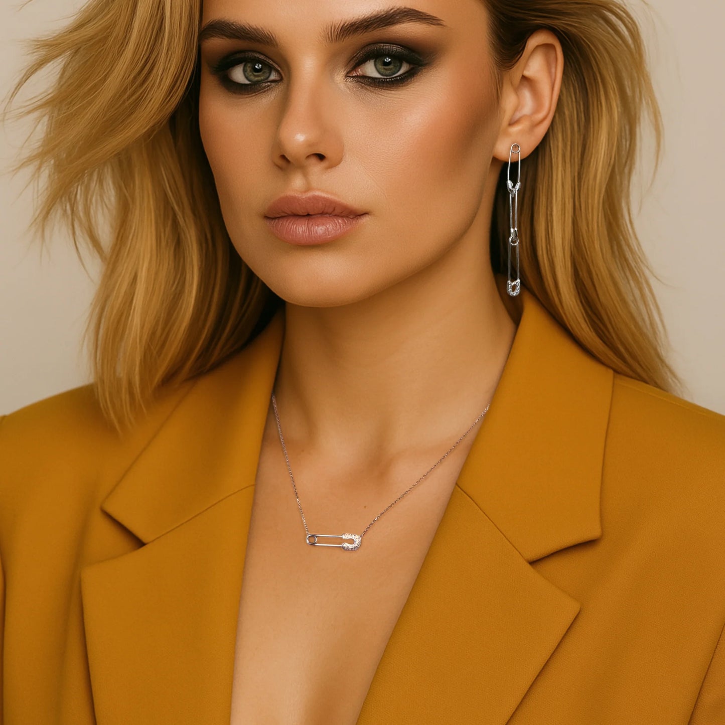 Fashionable blonde woman wearing matching safety pin long drop earrings and a delicate sterling silver necklace, styled with a mustard blazer and dramatic smoky eye makeup.