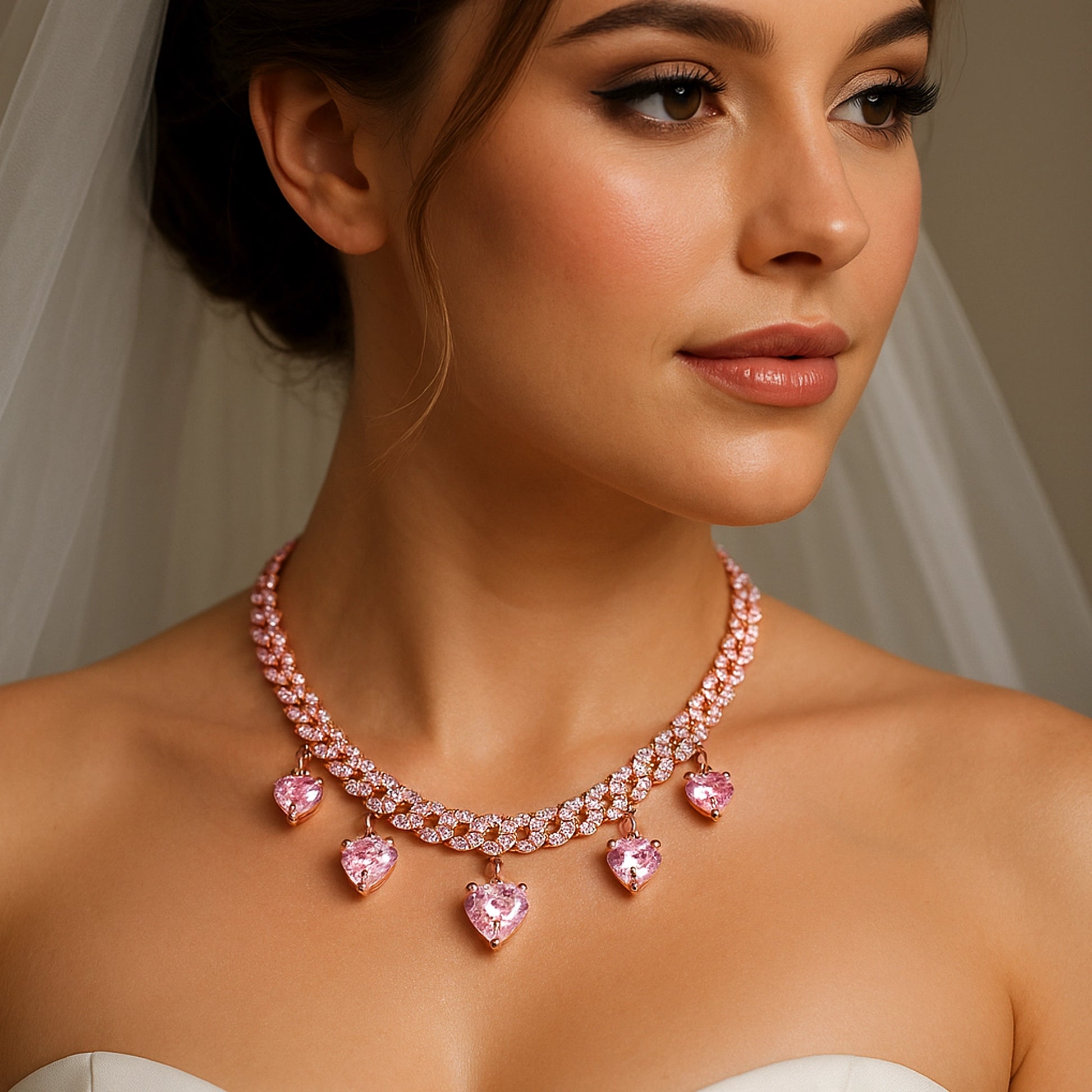 Bridal model wearing a double row rose gold curb chain necklace with pink heart cubic zirconia dangle charms and white pavé stones, styled with a strapless wedding gown and veil for an elegant bridal look.