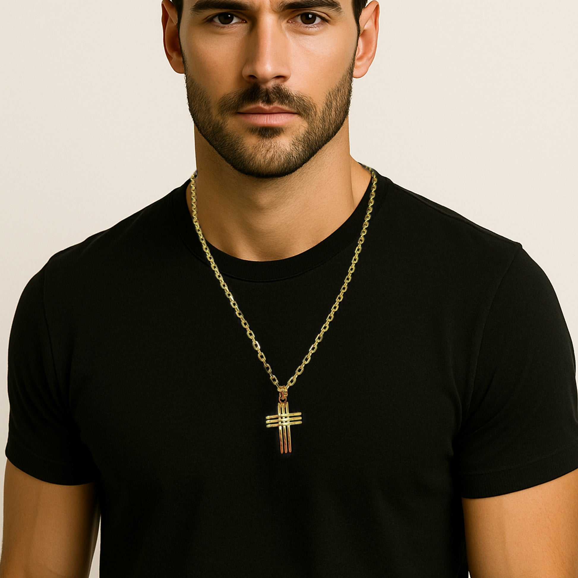 Portrait of a handsome man wearing a black fitted t-shirt and a bold 18k gold filled chain necklace with a curved dimensional cross pendant, styled against a clean white background.
