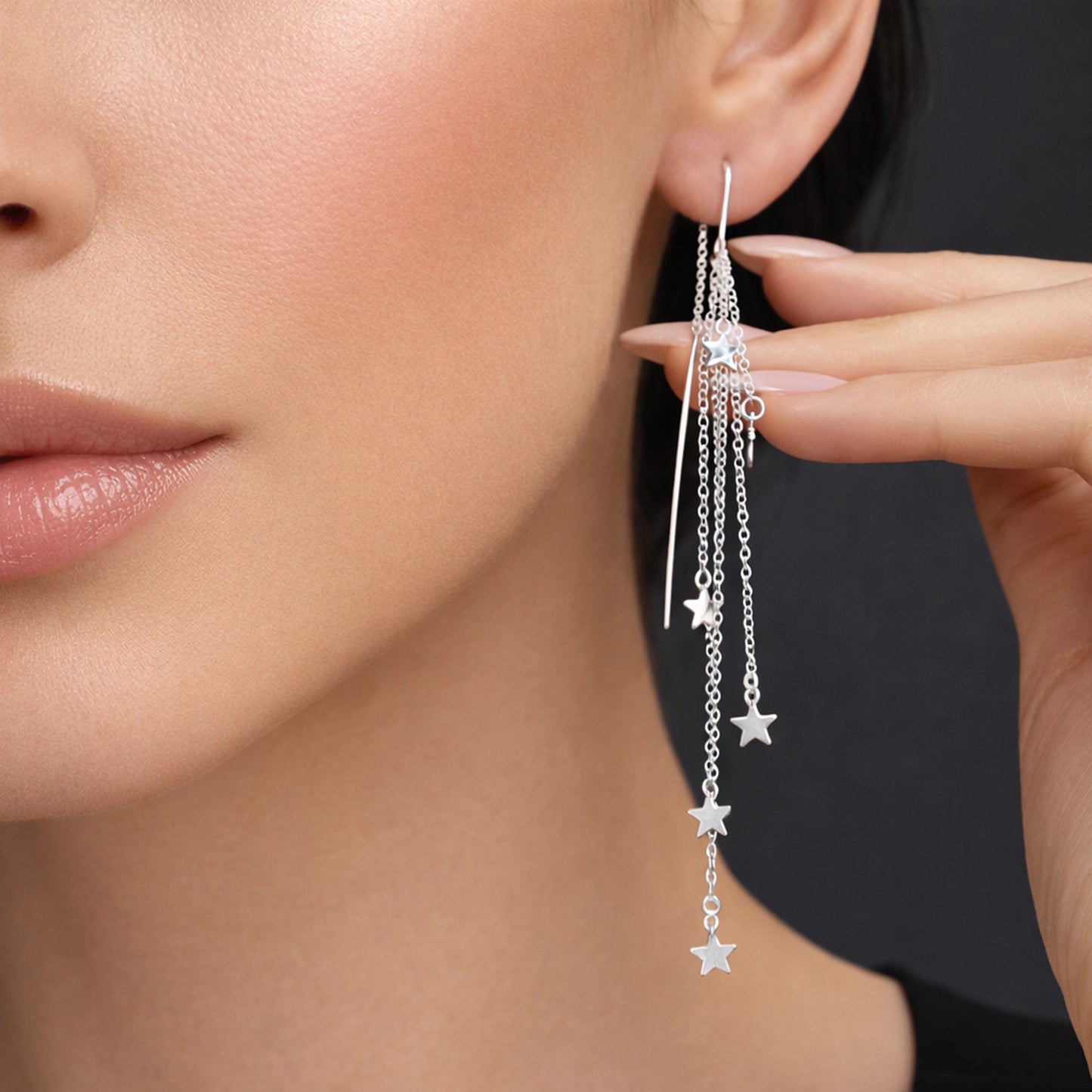 Sterling silver threader earrings with cascading star charms, worn in a close-up ear shot on a model with nude manicure. Long layered chain dangle earrings with polished silver stars, minimalist celestial jewelry, modern statement earrings for women.