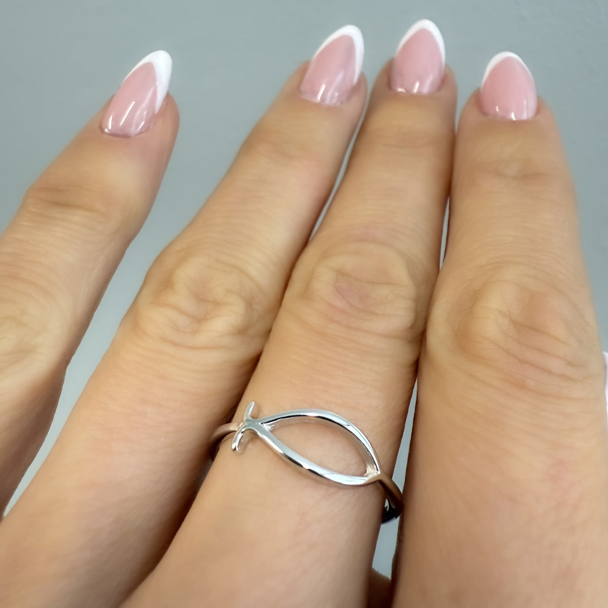 Hand wearing a delicate sterling silver Christian fish (Ichthys) ring, showcasing its minimalist and meaningful design against a neutral background.