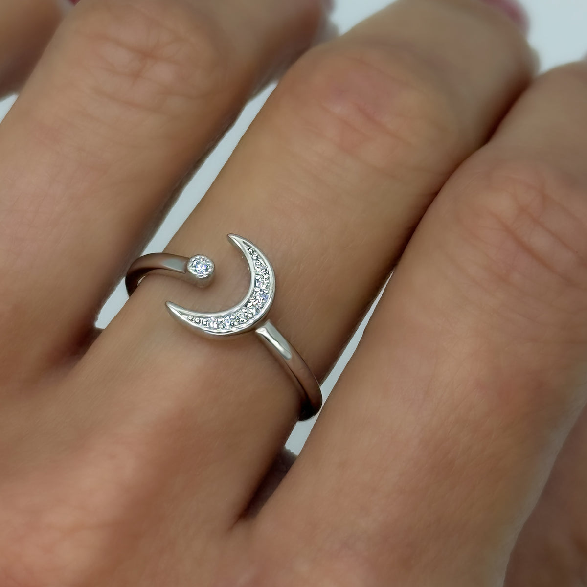 Close-up of a hand wearing a sterling silver open ring featuring a crescent moon design with cubic zirconia accents and a single CZ star tip. Adjustable and dainty celestial jewelry.