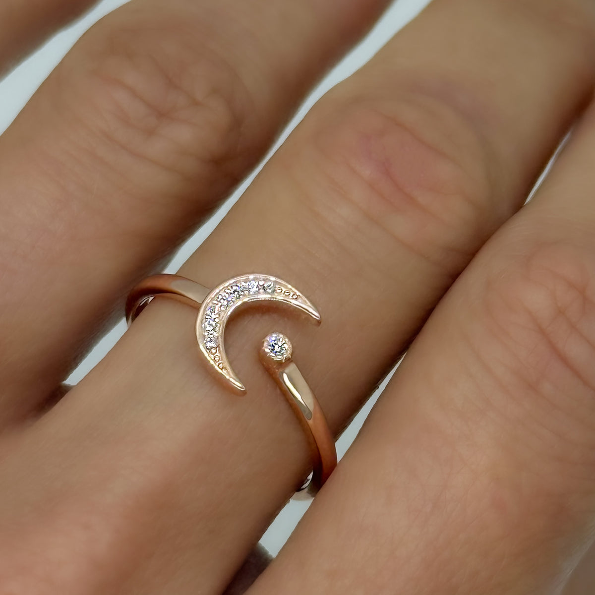 Rose gold vermeil crescent moon ring with CZ accents, shown on a hand. The open design wraps delicately around the finger with a tiny star detail. Elegant and adjustable celestial ring.