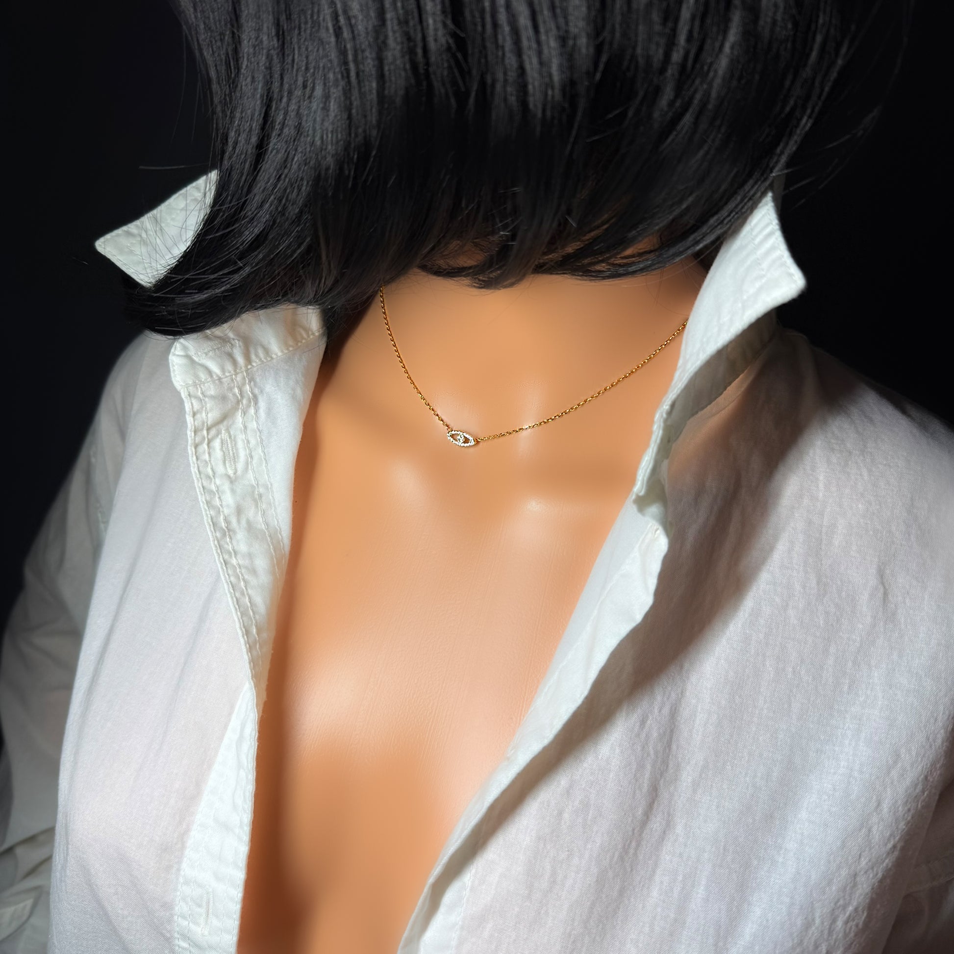 Dainty CZ evil eye gold necklace displayed on a mannequin with a white shirt, close-up view of the delicate gold chain and sparkling pendant.