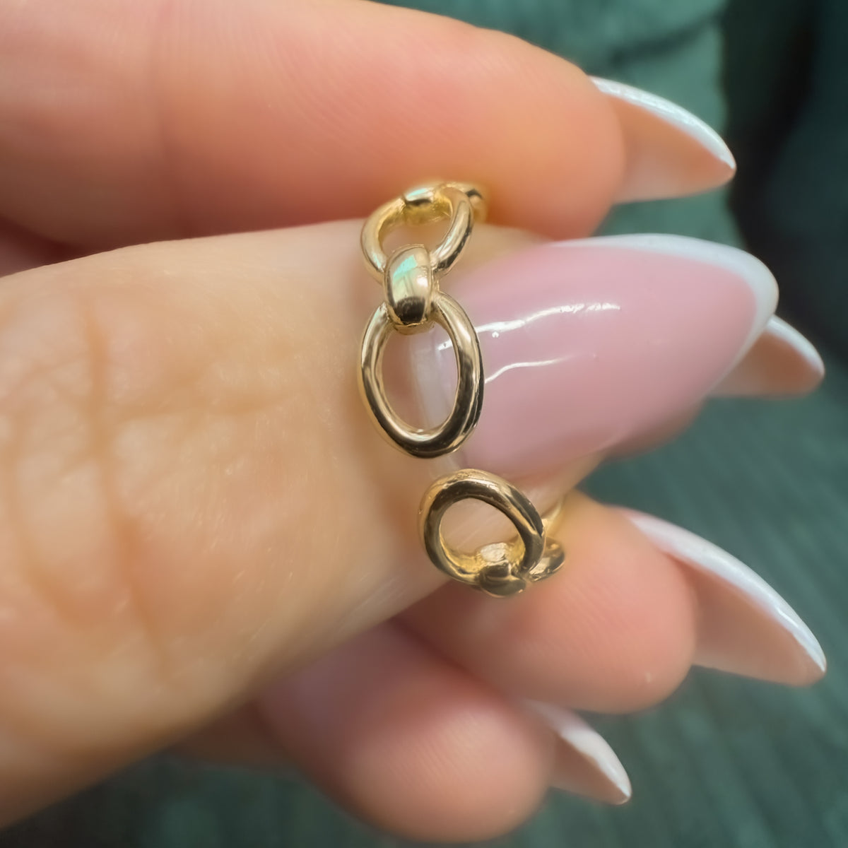Macro shot of a gold chain ring held between fingers, clearly showing the open adjustable gap between two links.


