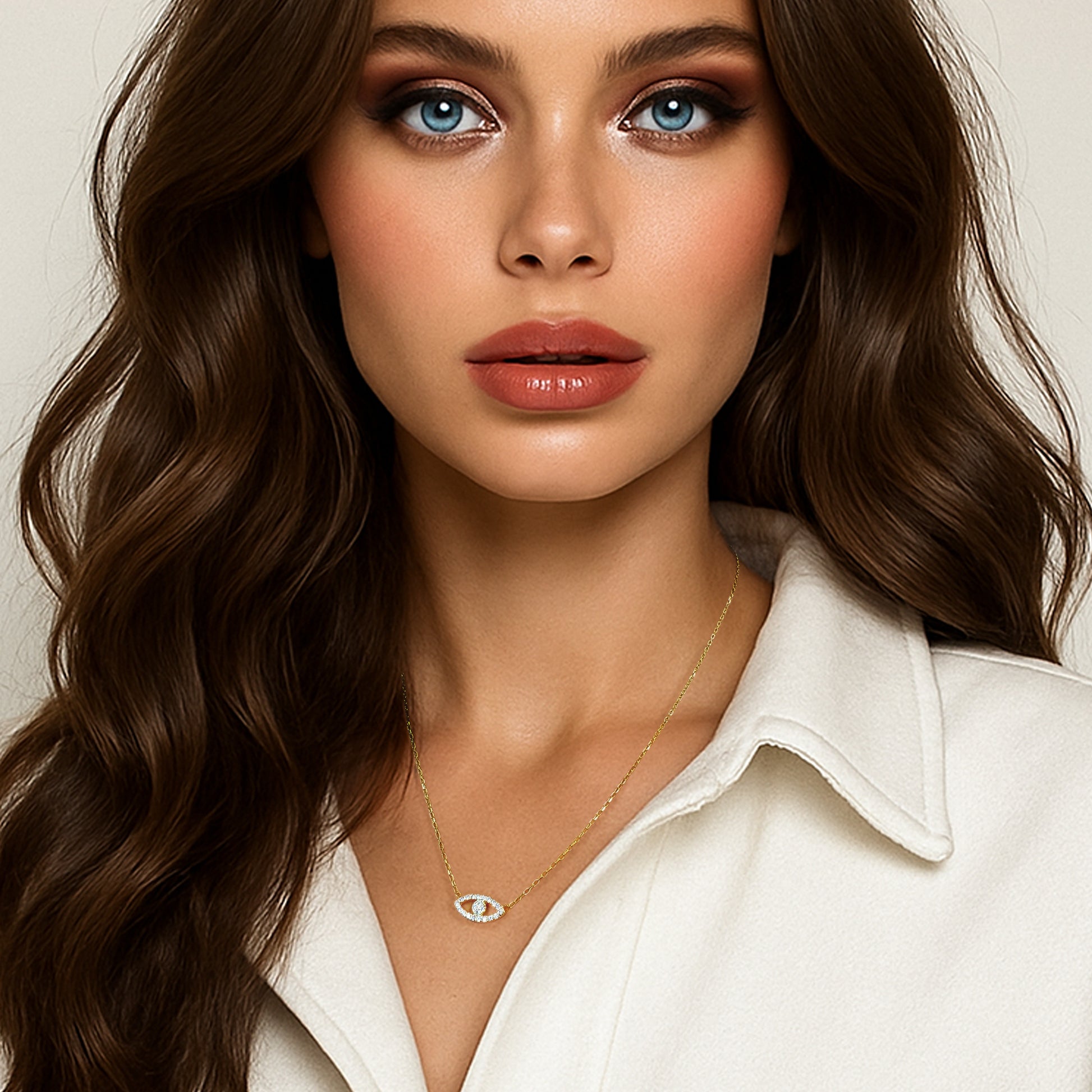 Elegant woman with wavy brunette hair and striking blue eyes wearing a white collared outfit and a delicate gold-plated sterling silver necklace featuring a CZ evil eye charm, styled for a sophisticated and protective look.