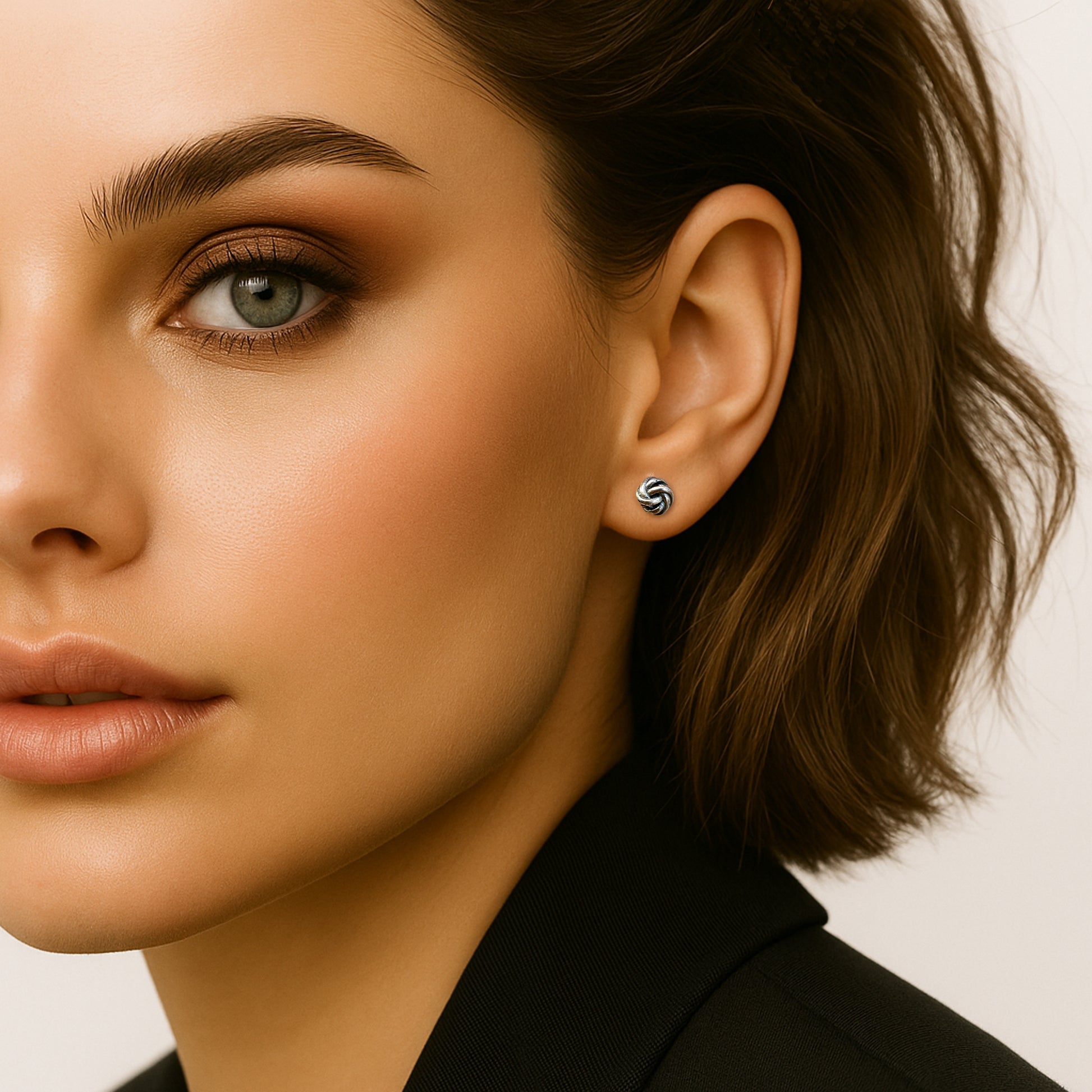 Delicate and sophisticated sterling silver love knot stud earrings worn by a woman with soft makeup and a stylish bob haircut.