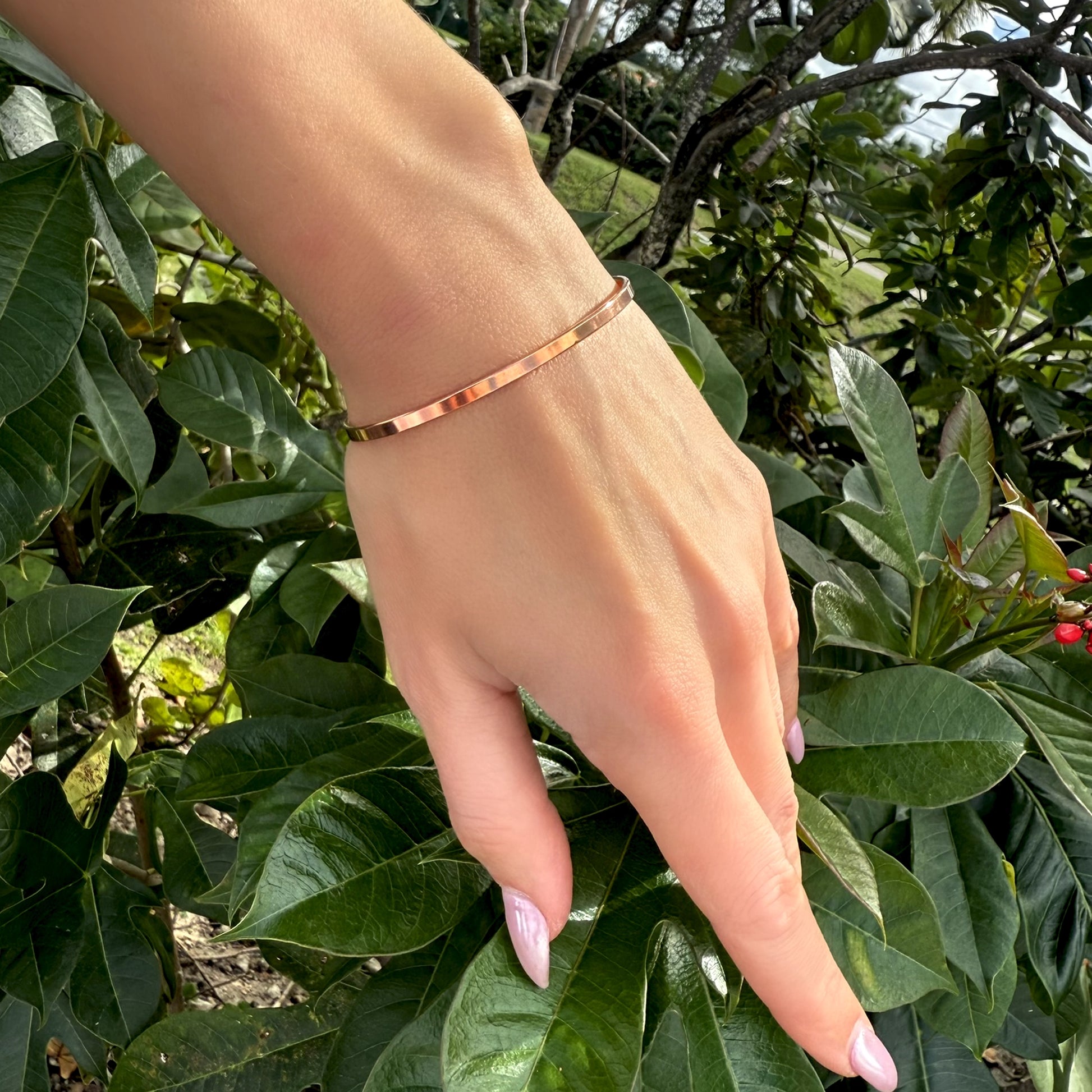 Hand wearing a copper bracelet with green foliage in the background